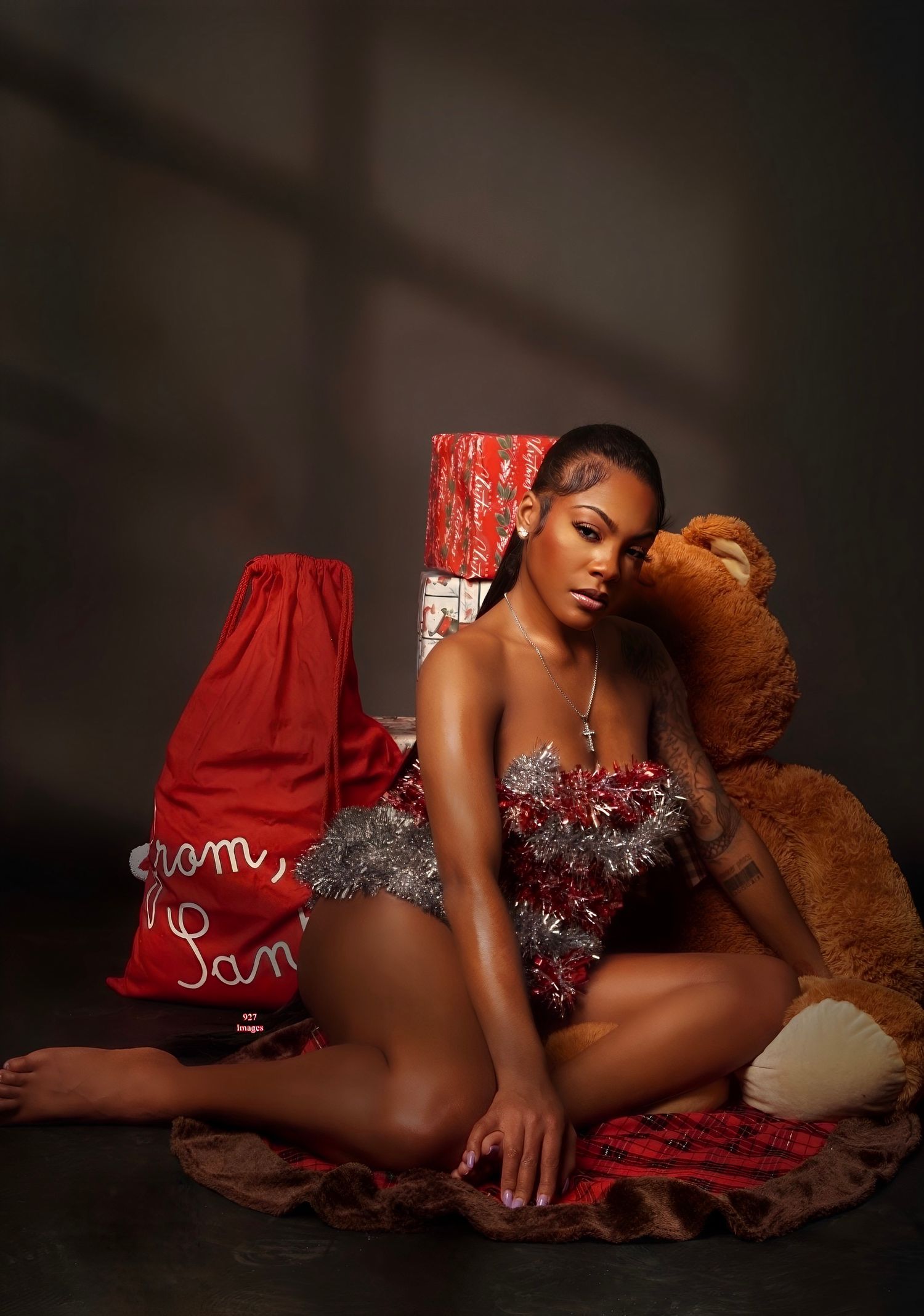 Woman in festive silver holiday outfit posing with teddy bear and Christmas gifts in studio setting.