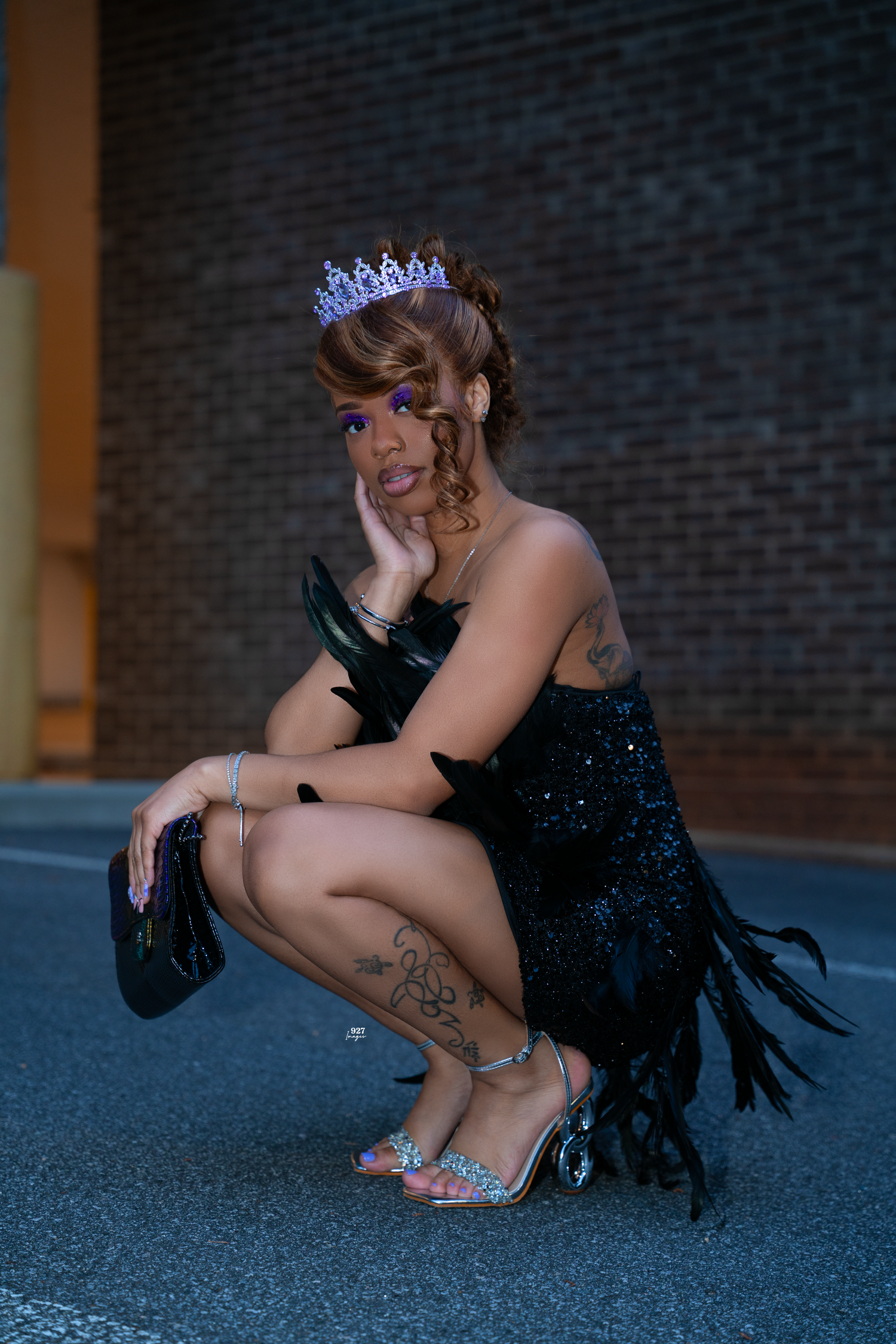 Woman in black sequin fringe dress and tiara crouching dramatically on urban street at night.