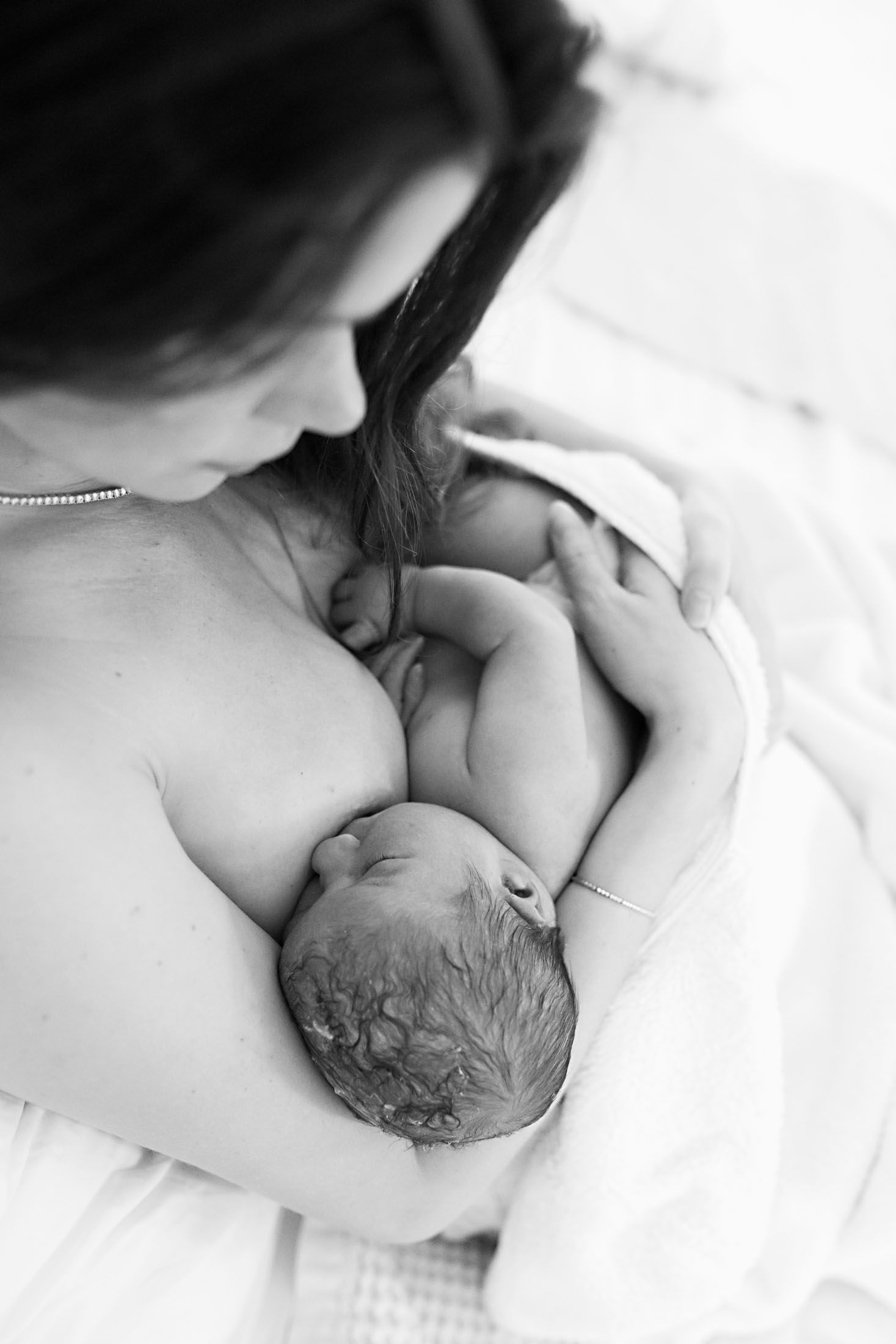 A mother gazes lovingly at her newborn baby while breastfeeding in a serene black and white close-up photo.