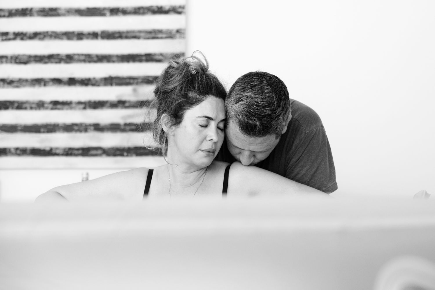 A couple shares a tender embrace in a birthing pool as the woman labors during a home water birth.