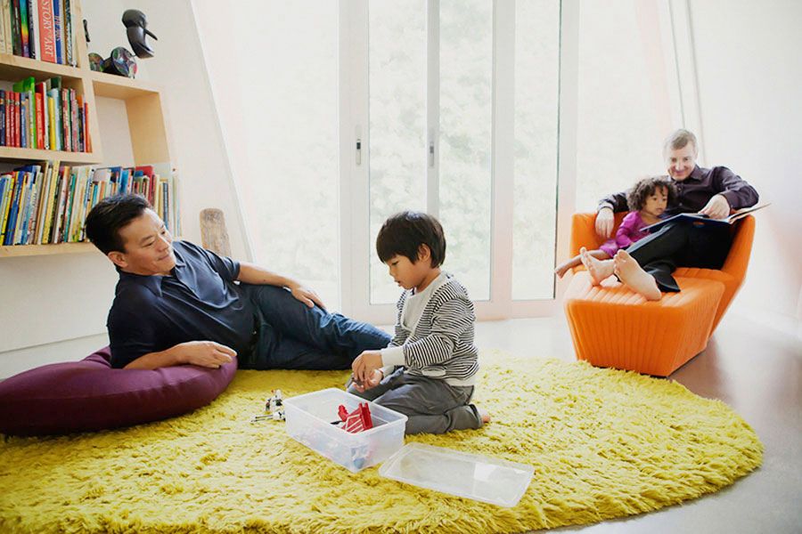 Family relaxing in a modern living room with yellow rug, child playing with toys on floor.