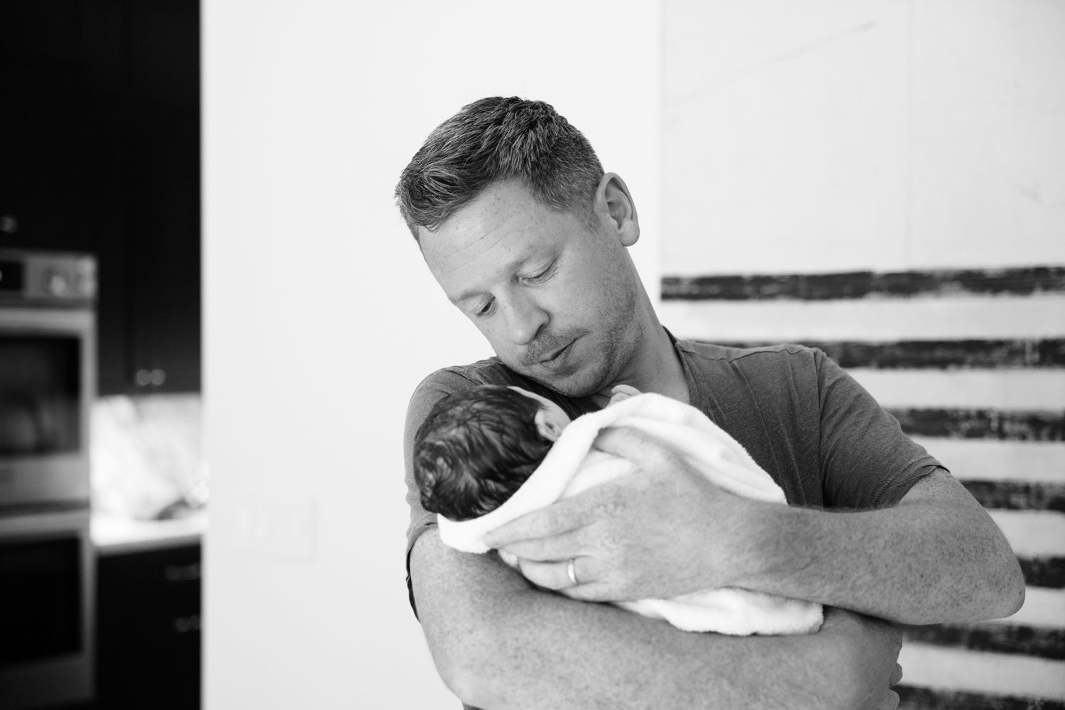 New father tenderly cradles sleeping newborn wrapped in white towel against his chest after birth.