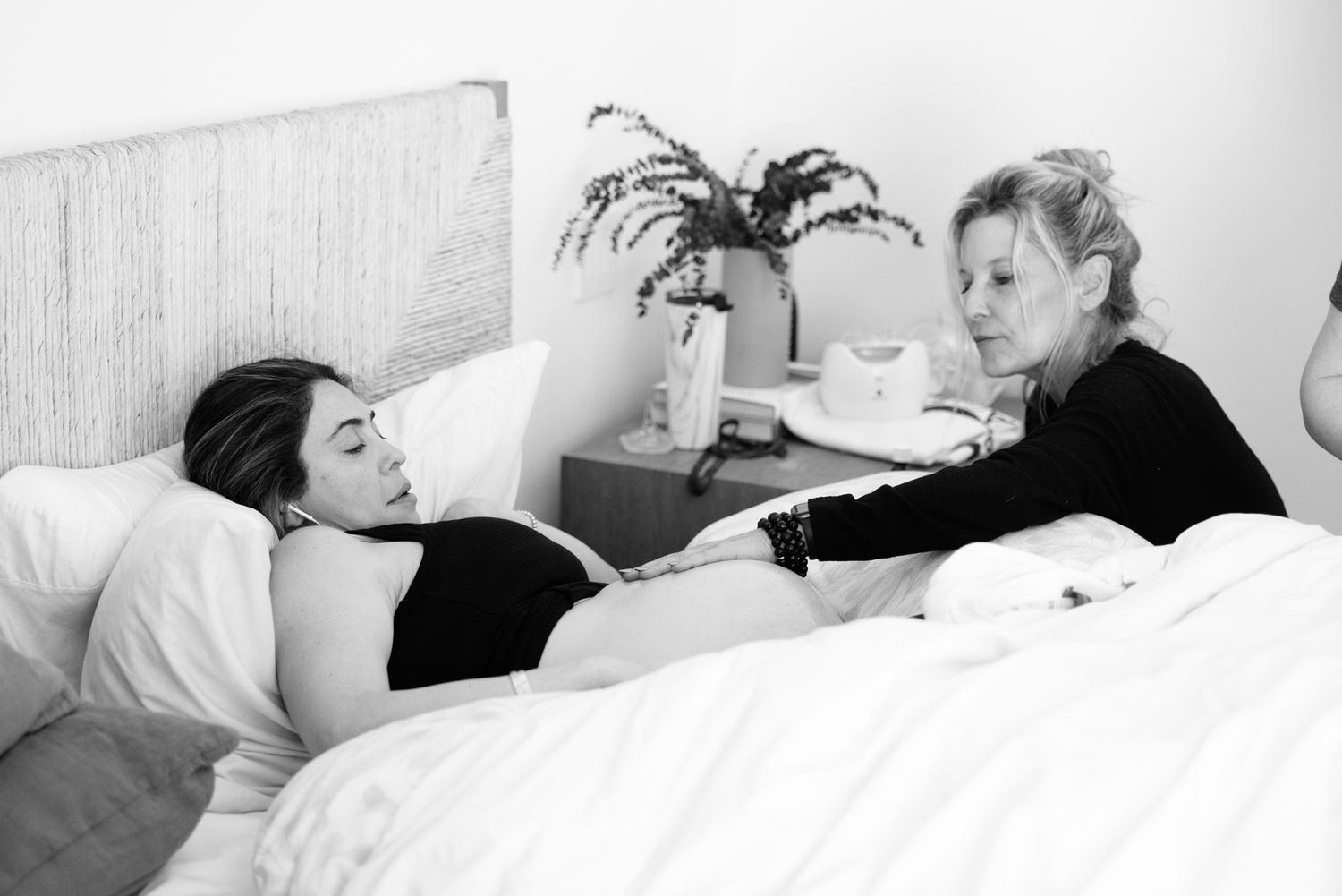 Pregnant woman lying in bed while doula provides calm, attentive prenatal support.