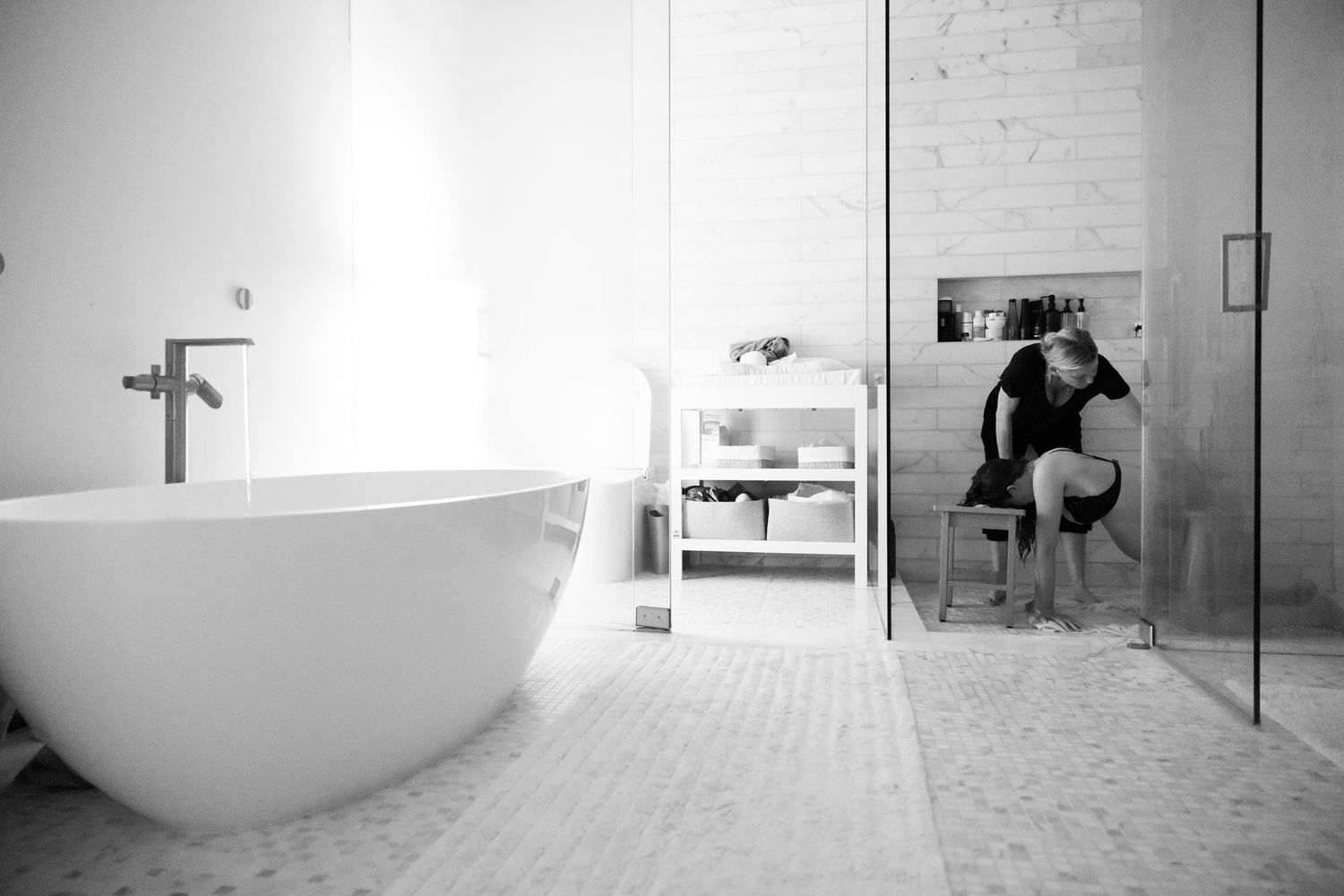 Pregnant woman sitting in bathroom near freestanding white bathtub during labor.