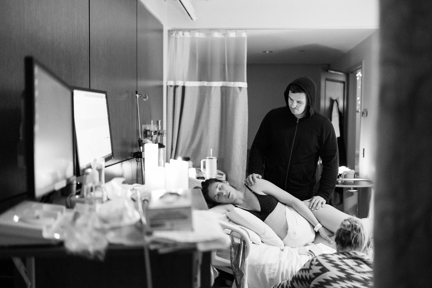 Black and white photo of a pregnant woman lying in a hospital bed with a caregiver standing beside her.