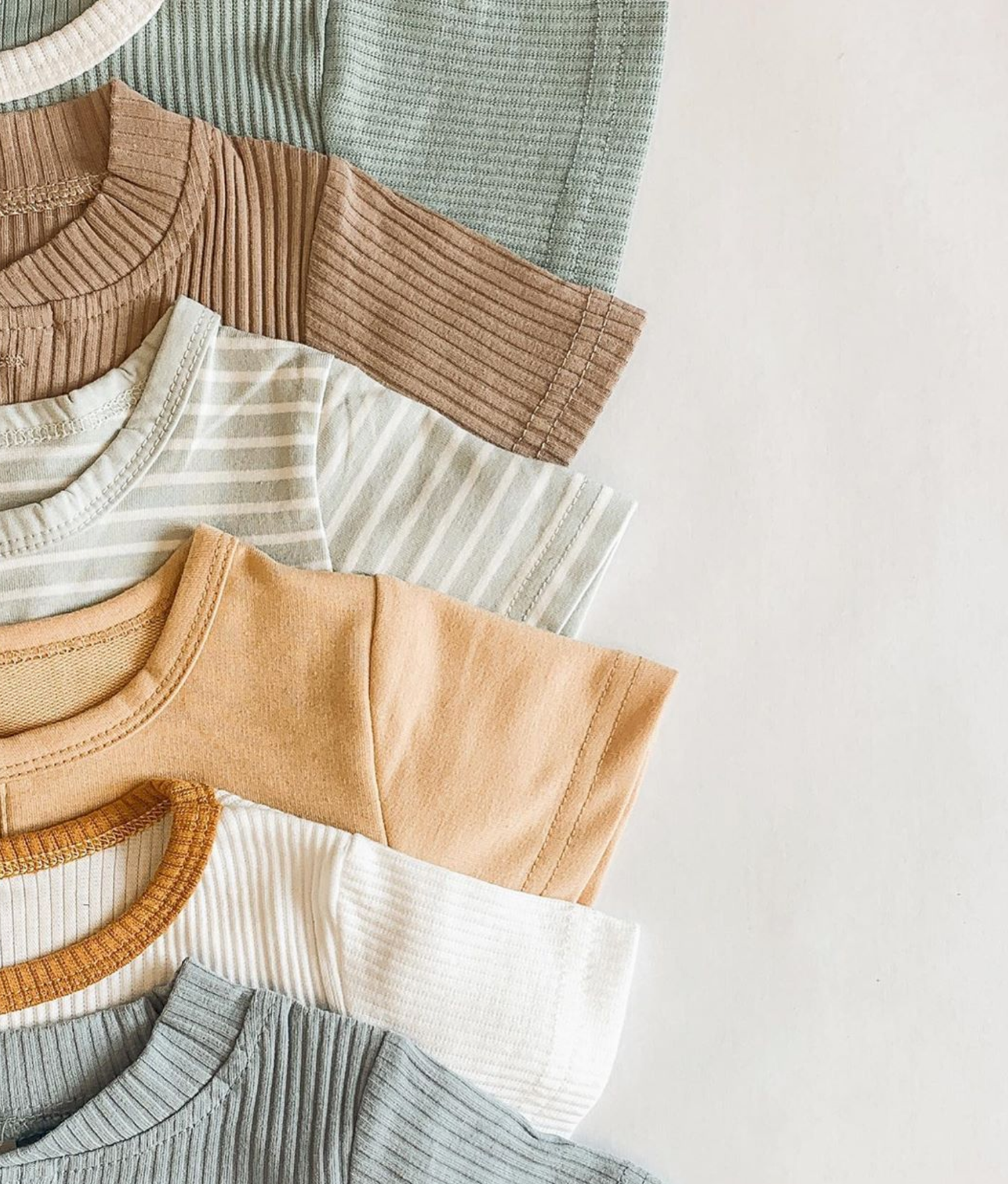Stack of colorful ribbed and striped baby onesies in neutral tones including sage, tan, cream, and blue.