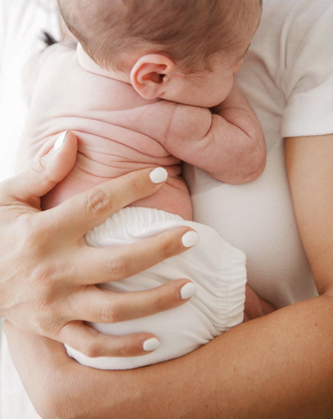 A parent gently holds a newborn baby in a white diaper against their chest, showcasing a tender bonding moment.