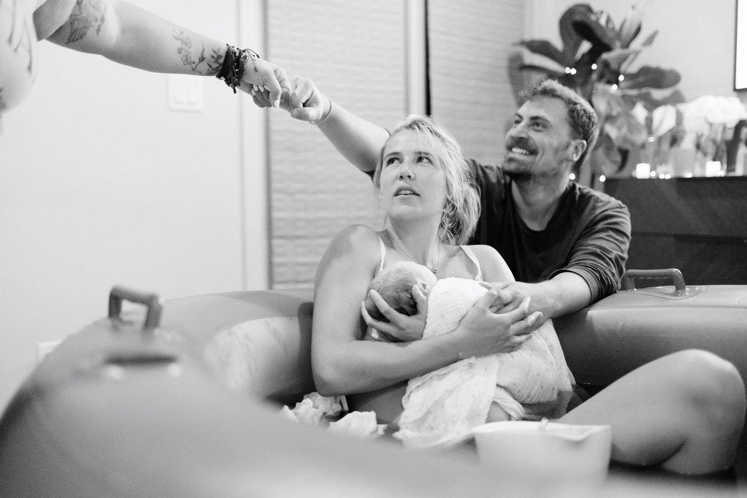 Black and white photo of a couple sitting on a couch, smiling and holding a newborn baby.