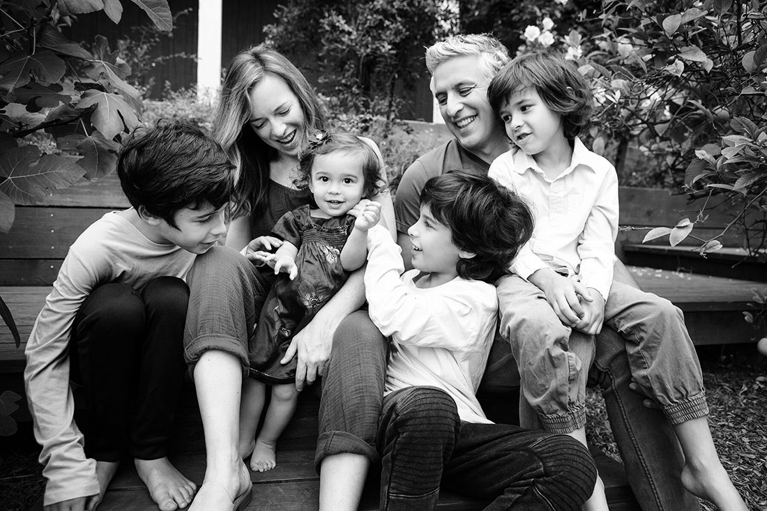 Black and white photo of two women smiling with four young children sitting together outdoors on steps.