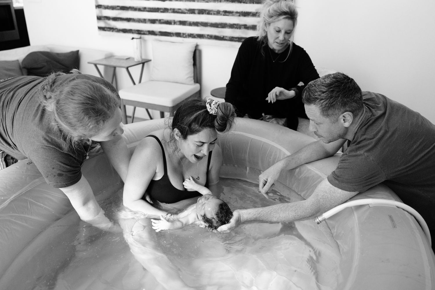A joyful moment as a newborn is lifted from the water surrounded by a loving birth team during a home water birth.