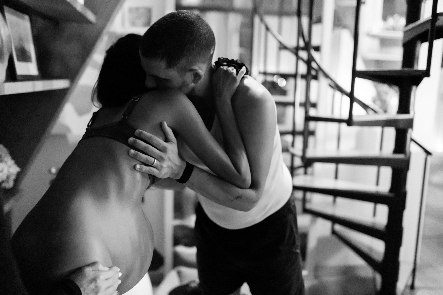 Black and white photo of two people sharing an emotional embrace indoors.