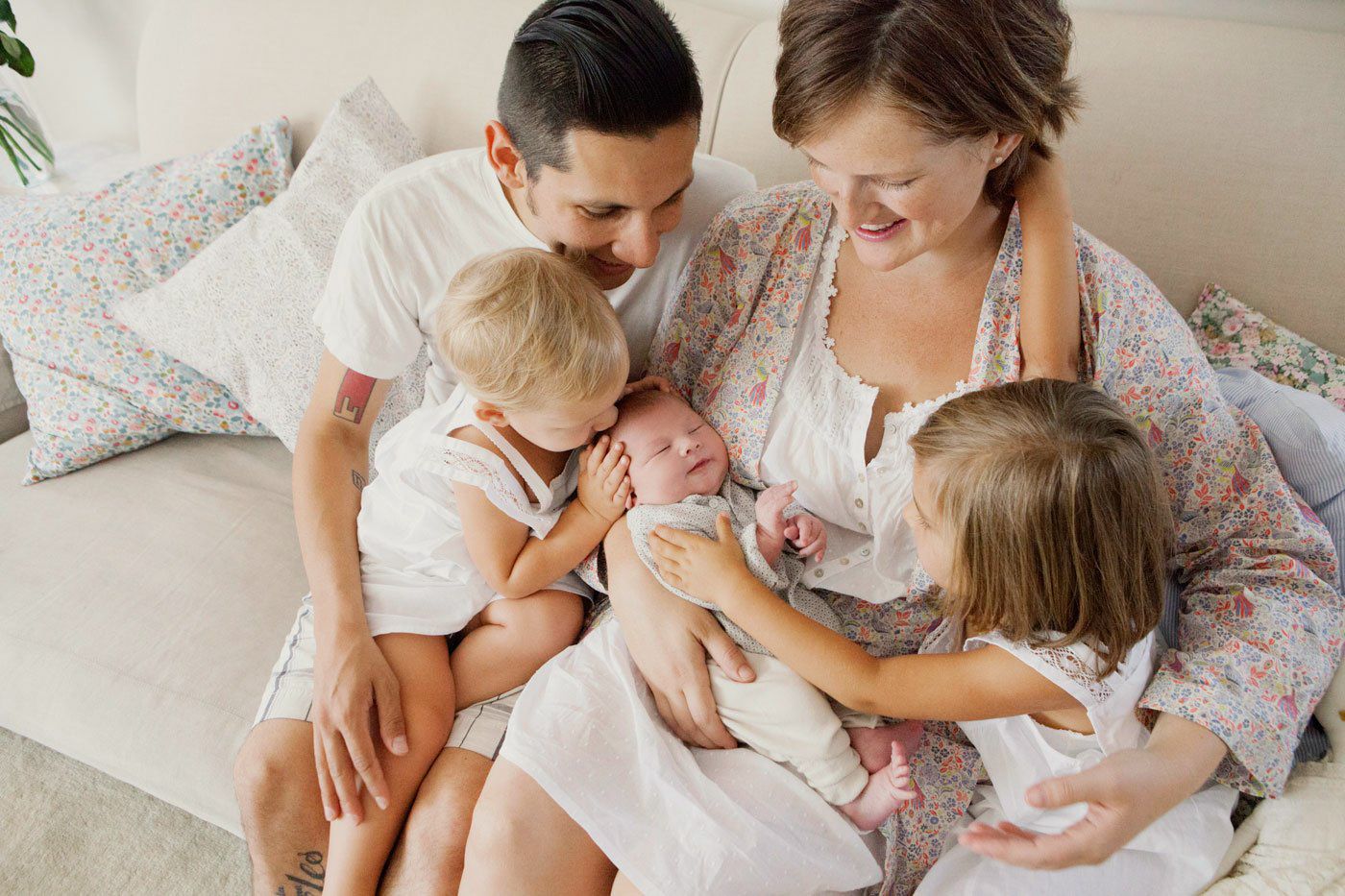 Happy family of five with parents and three young children, including a newborn baby, sitting together on a cozy sofa.