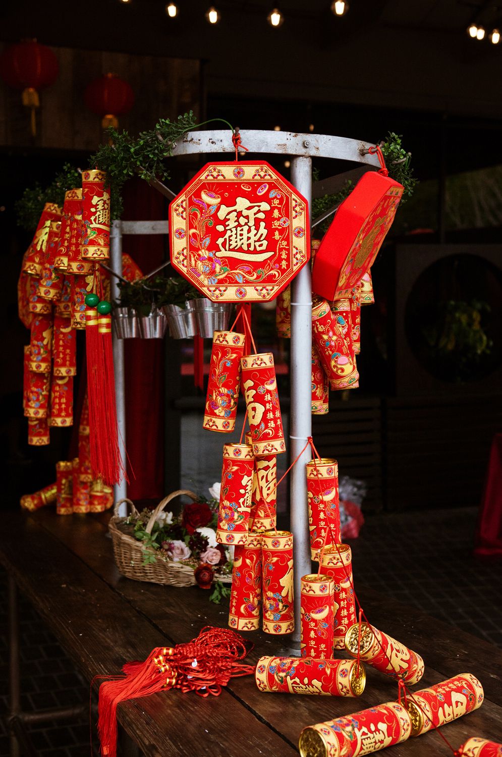 Decorative red and gold Chinese firecracker ornaments and lucky charms displayed on a wooden stand at a festival.
