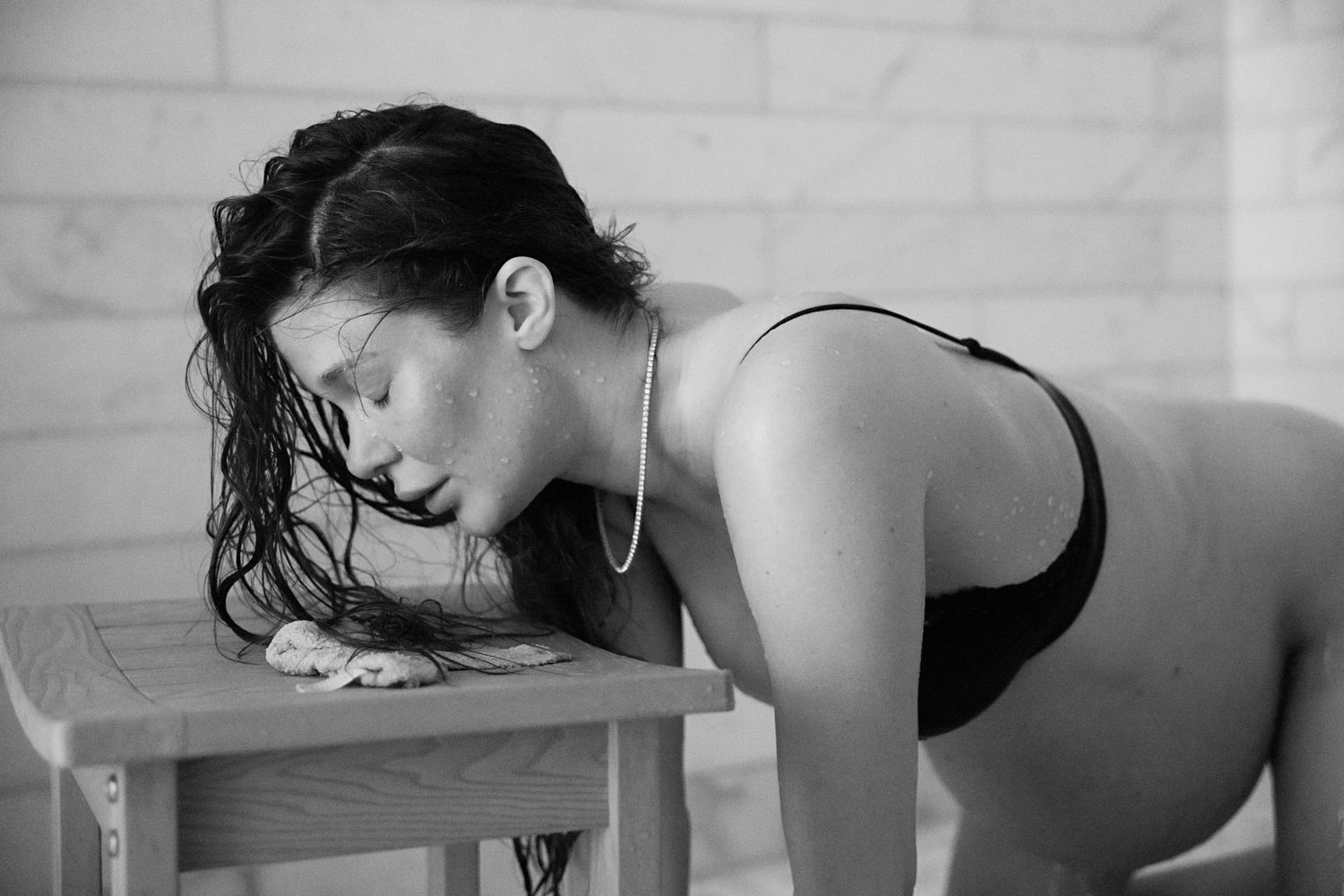 Pregnant woman in black swimsuit resting head on wooden stool during labor.
