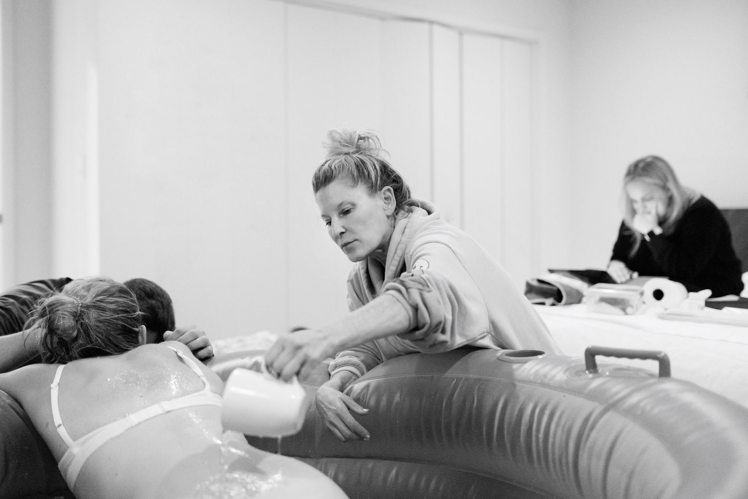 Midwife assisting woman during active labor in inflatable home birthing pool.