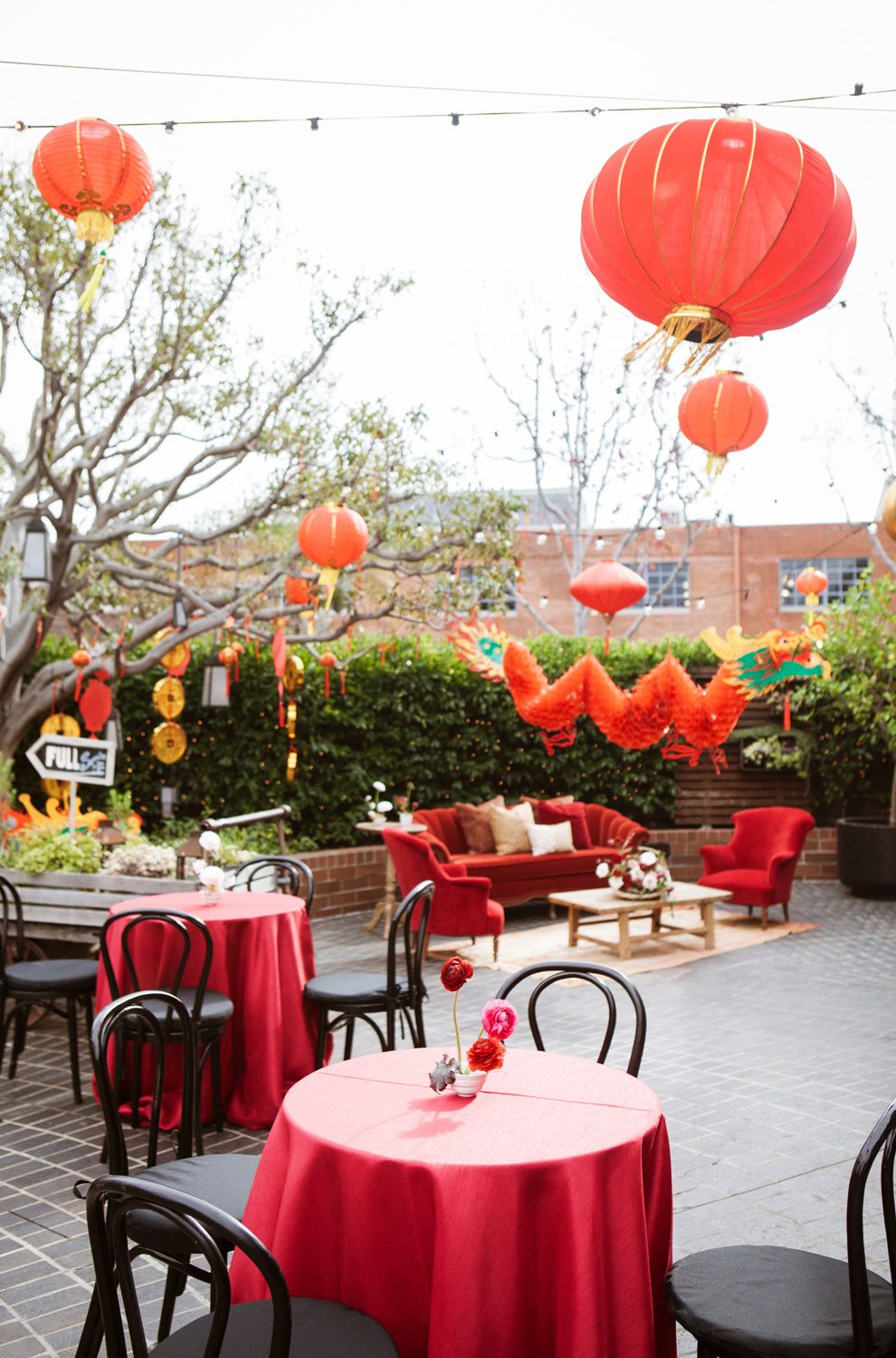 An outdoor party venue decorated with red Chinese lanterns and red tablecloths for a festive celebration.