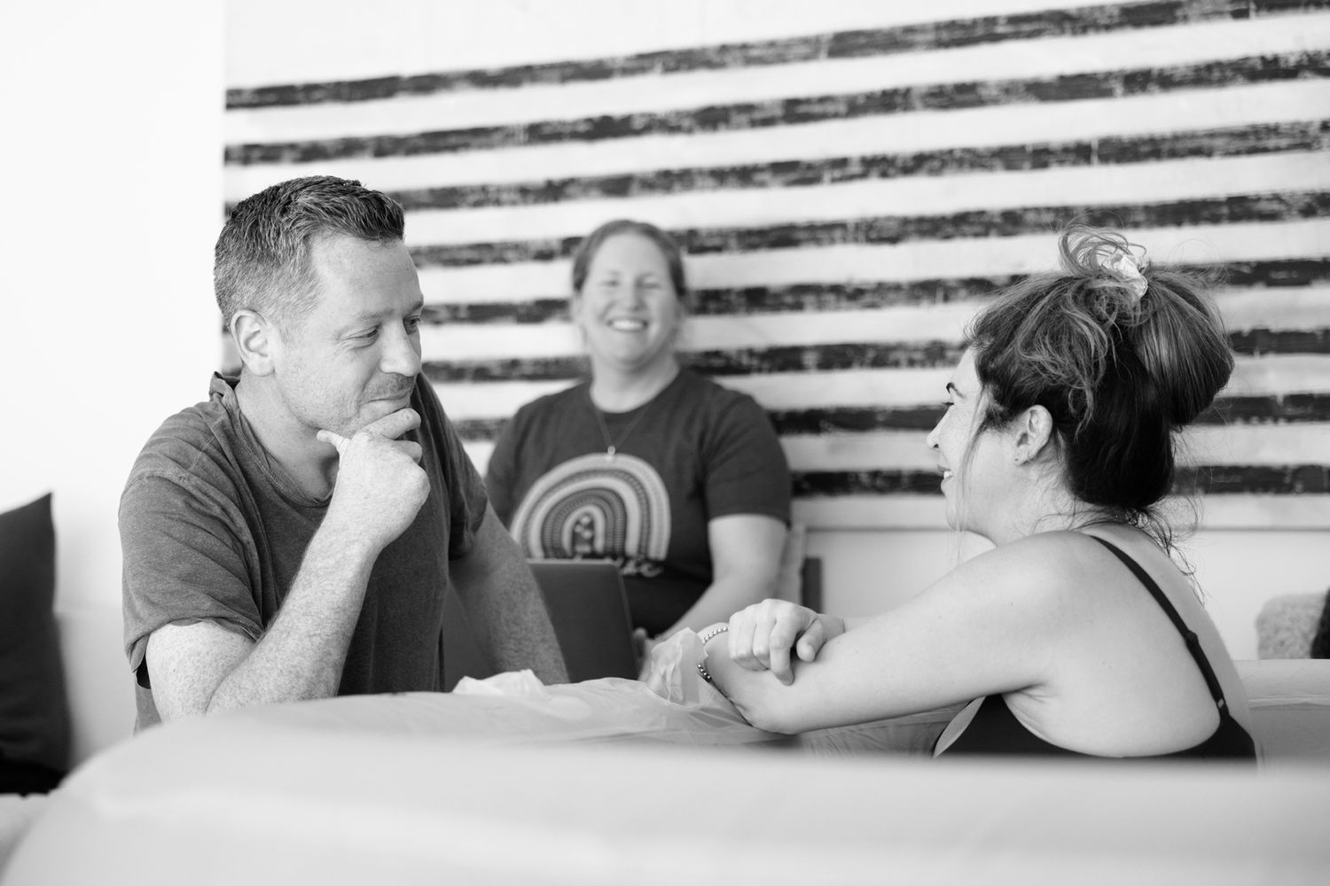 A man and pregnant woman share a conversation at a table while a smiling person looks on during a home birth consultation.