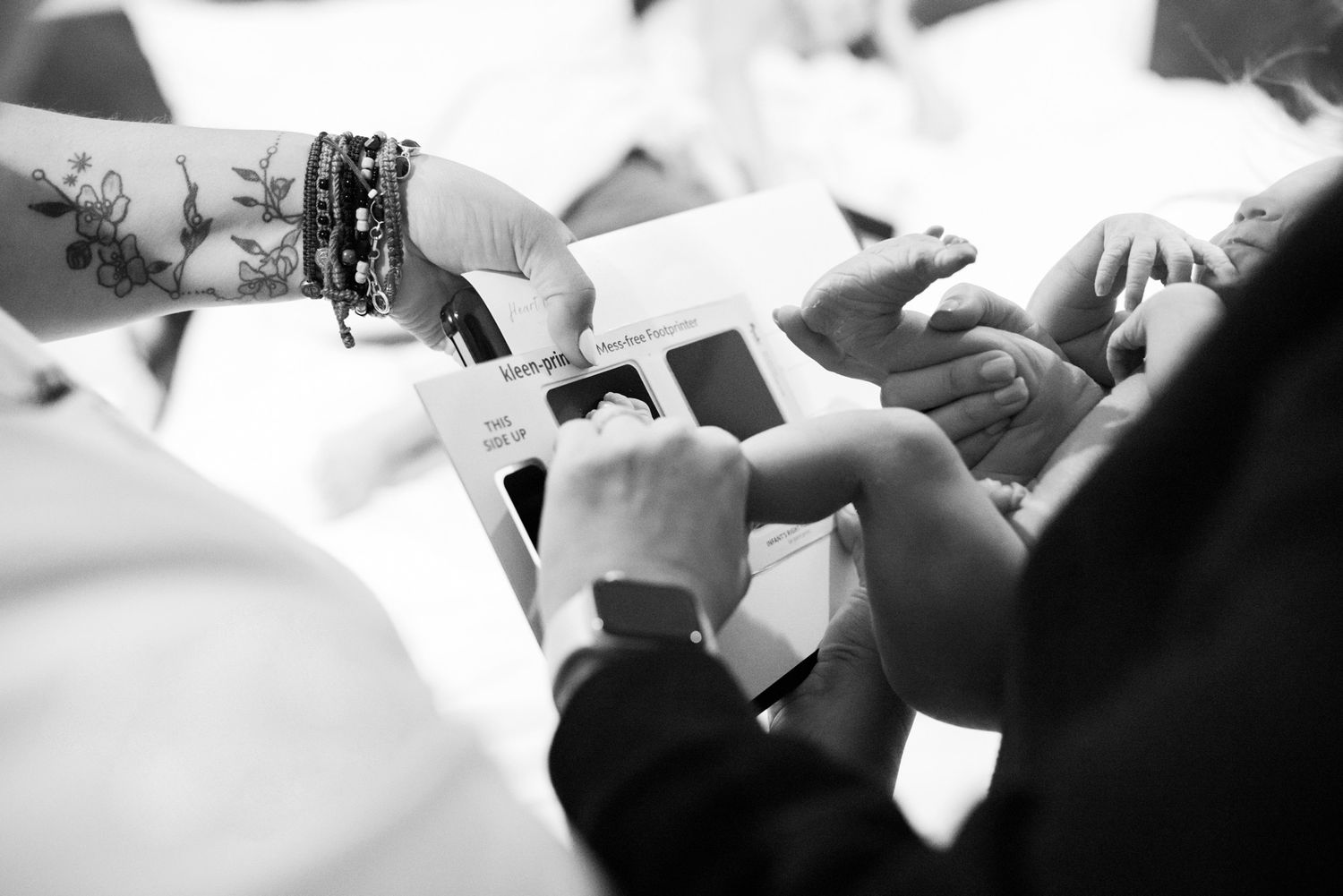 Close-up of hands sharing ultrasound photos, black and white image with visible tattoo and watch.