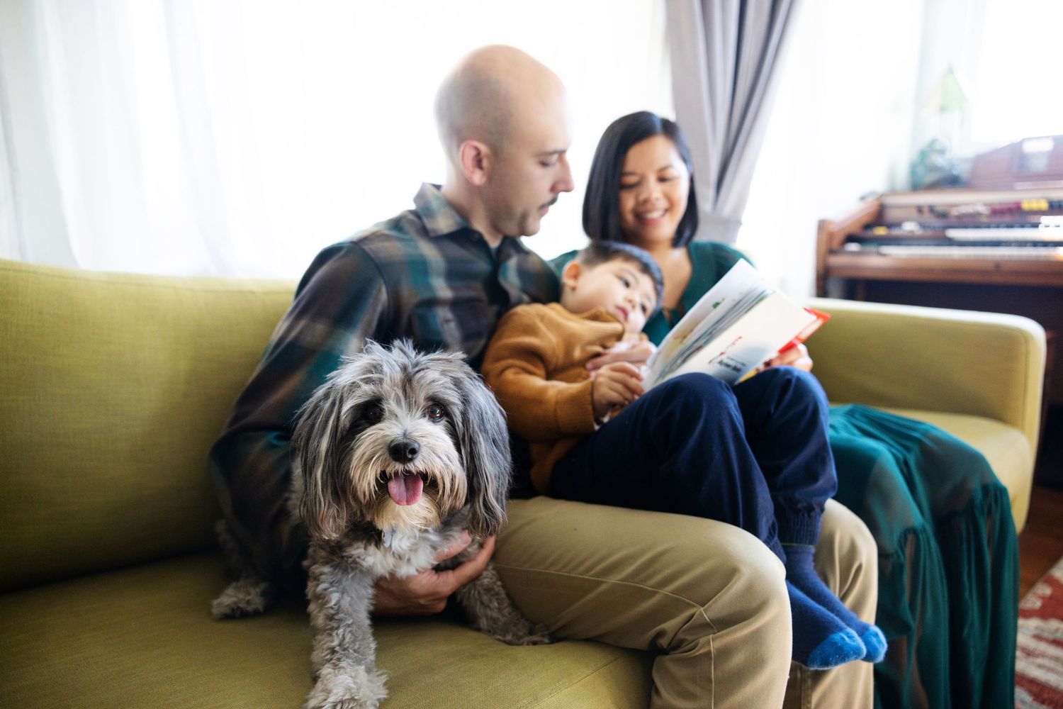 Happy family with a fluffy dog relaxing on a couch reading a book together at home.