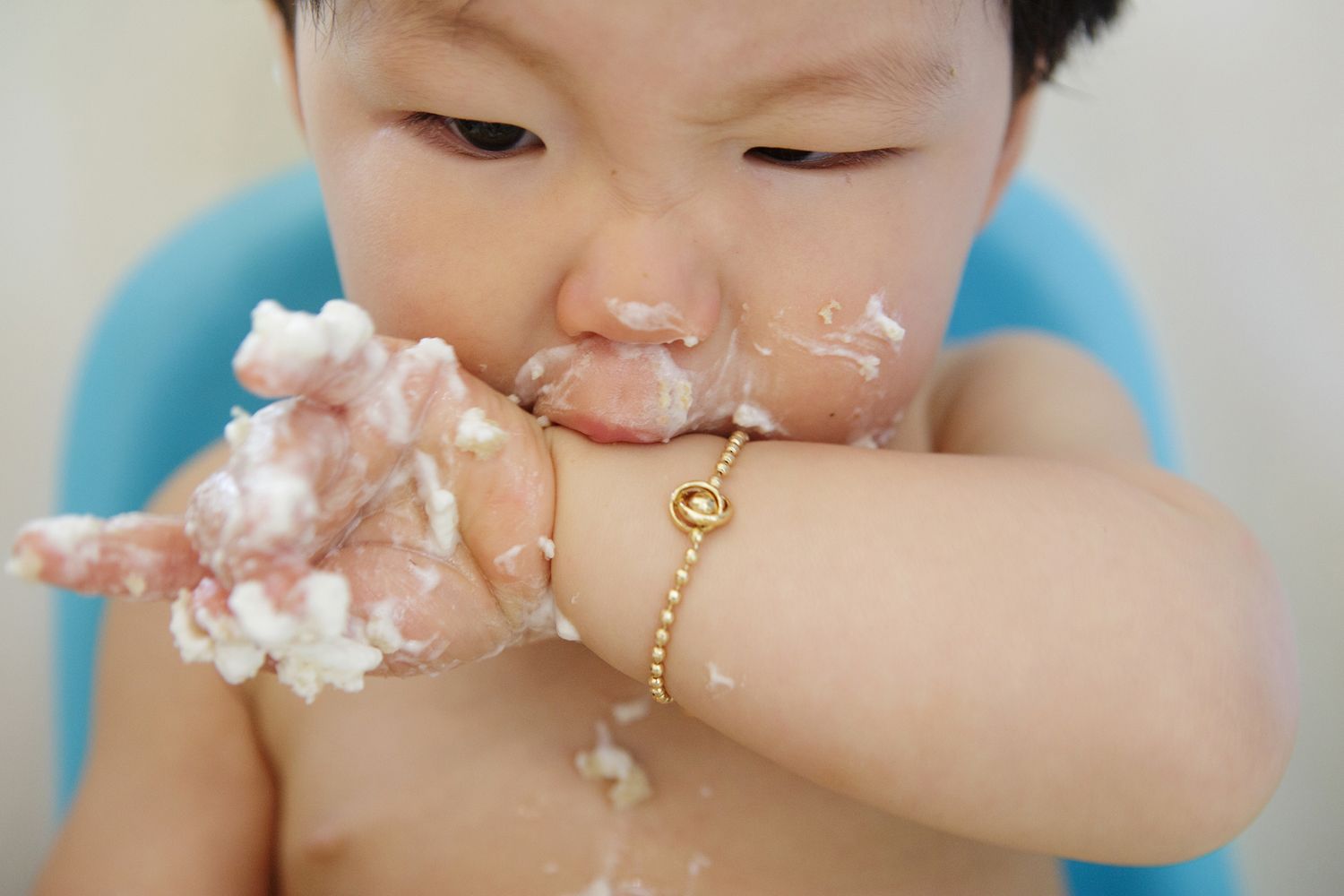 Asian baby with cake smeared on face and hands during first birthday smash cake celebration.