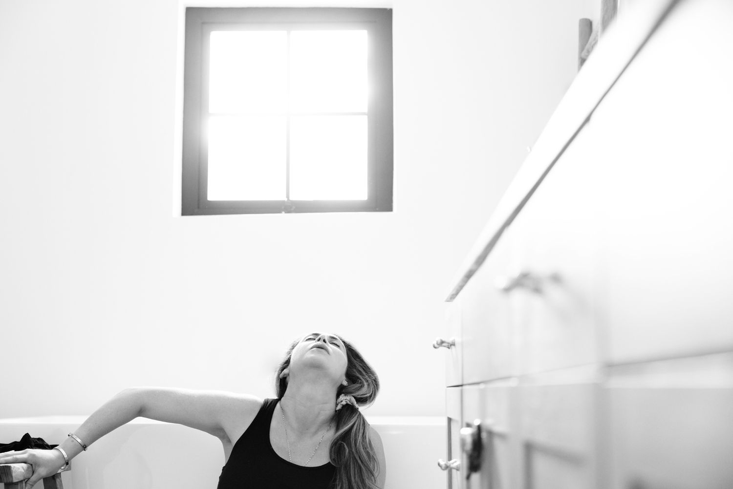 A woman tilts her head back during labor in a bright white bathroom.