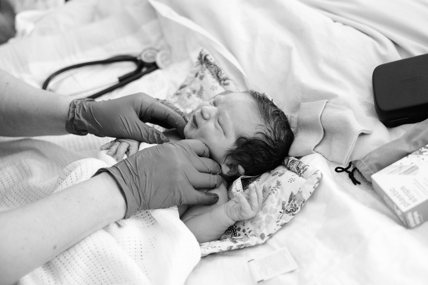 Black and white photo of a newborn baby being examined by a gloved healthcare professional after birth.