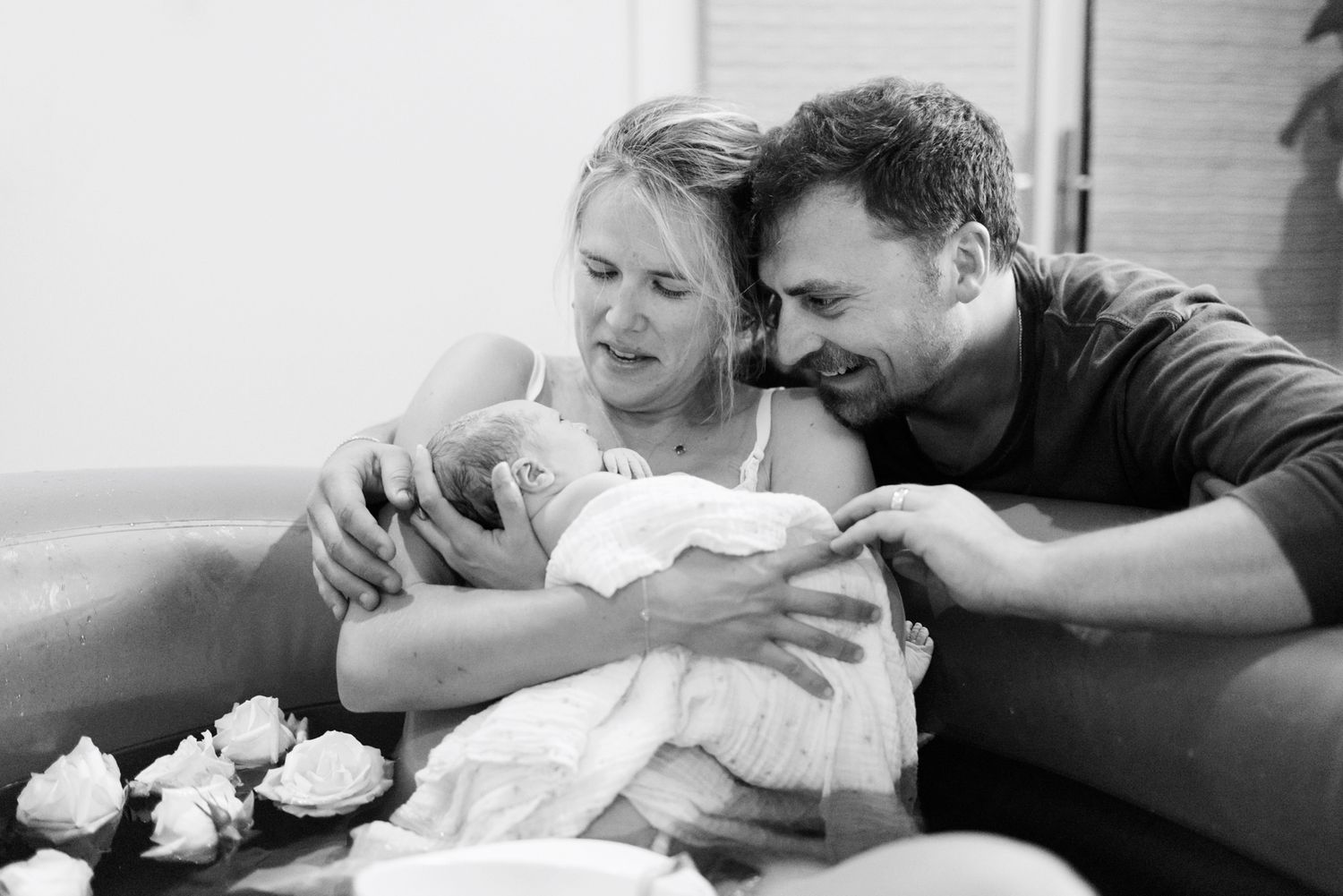 Black and white photo of new parents smiling and bonding with their newborn baby after a home water birth.