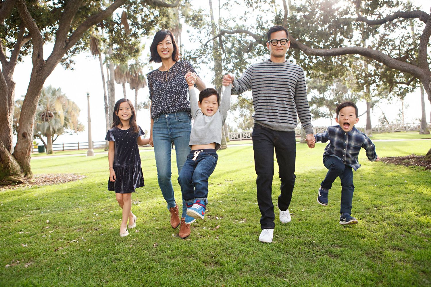 Happy Asian family holding hands and swinging children in a sunny park.