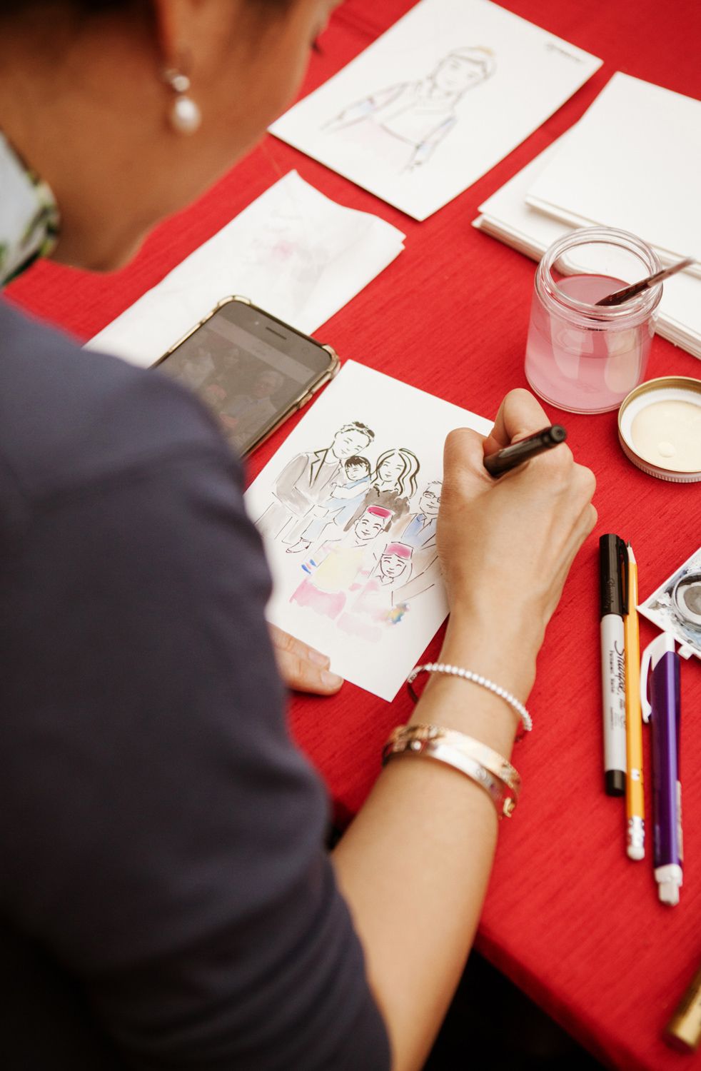 An artist creates a colorful caricature illustration at a red-covered table during a festive celebration event.