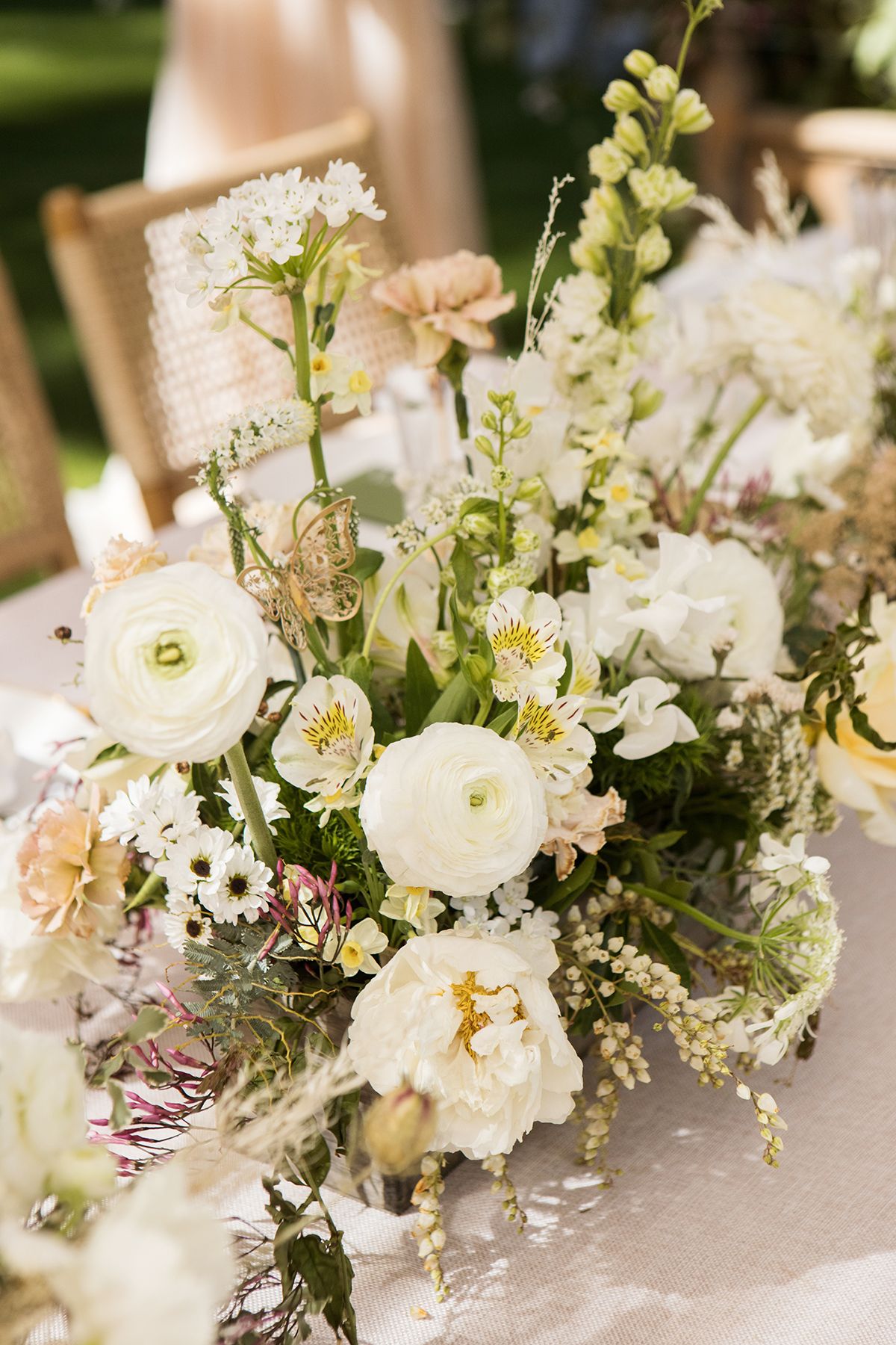 Elegant wedding centerpiece featuring white ranunculus, peonies, and mixed blooms on a linen tablecloth.