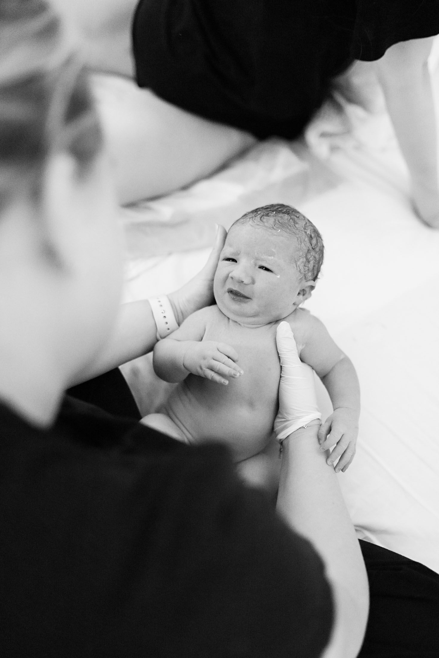 A smiling newborn baby is held by a nurse or midwife in a black and white hospital photo.