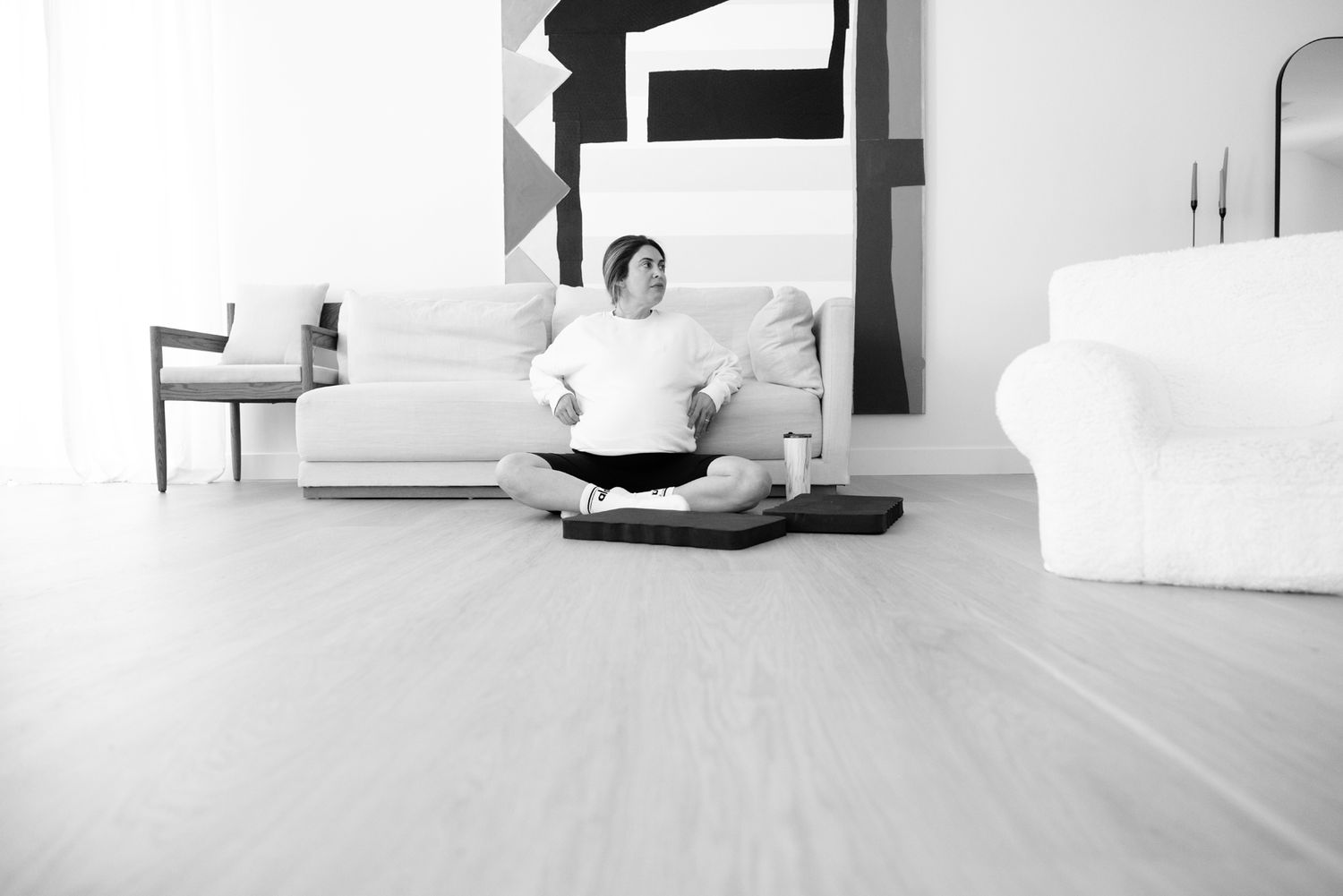 Pregnant woman sitting cross-legged on floor meditating calmly in bright modern living room.