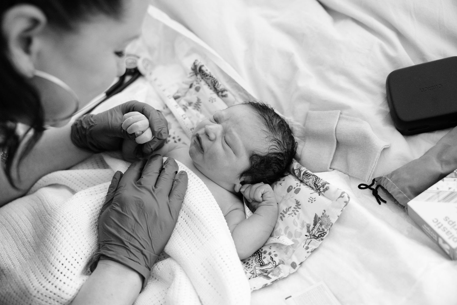 Midwife and mother admire peaceful sleeping newborn wrapped in blanket during postnatal checkup.