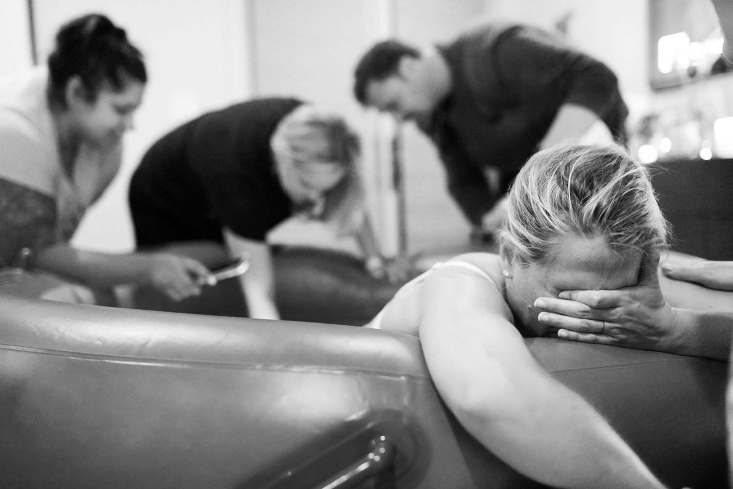 Black and white photo of a woman laboring in a birth pool with support team assisting during home water birth.