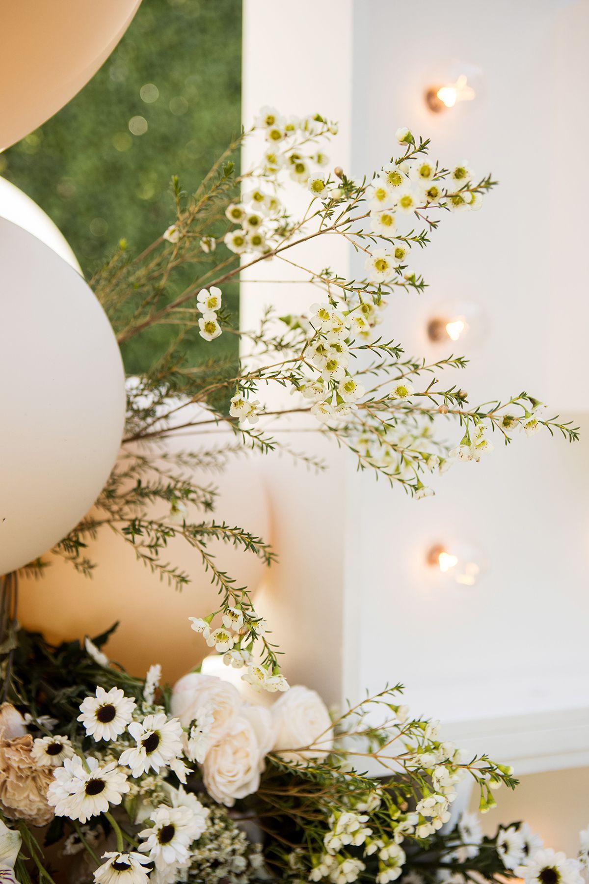 White wedding floral arrangement featuring delicate wildflowers, white roses, and daisies with warm glowing lights in background.