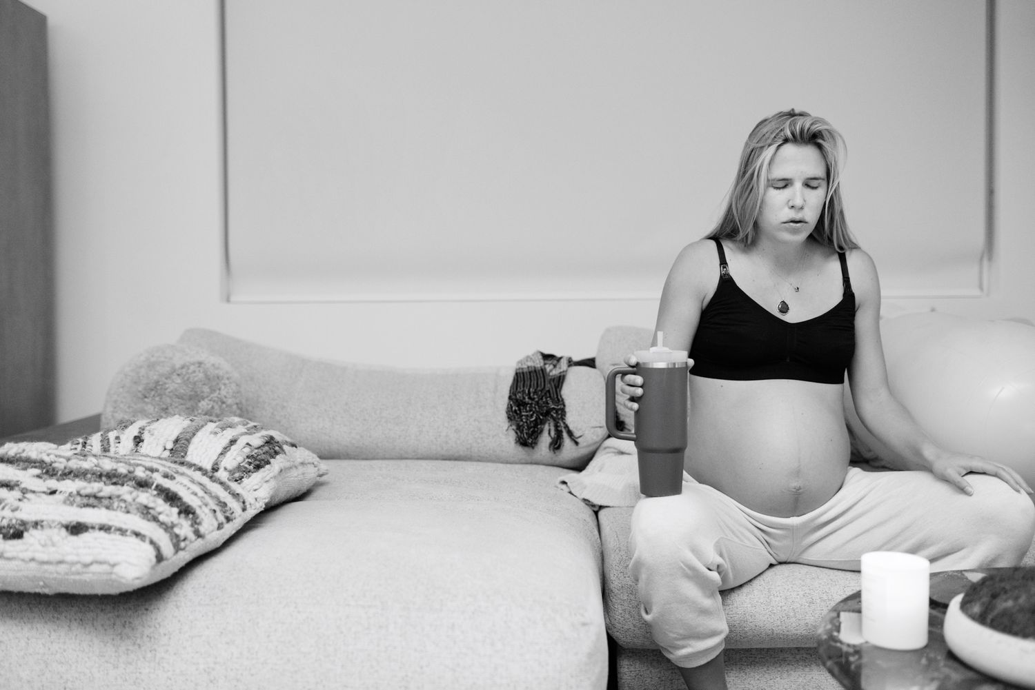 Pregnant woman sitting on floor examining baby shoes in black and white home setting.