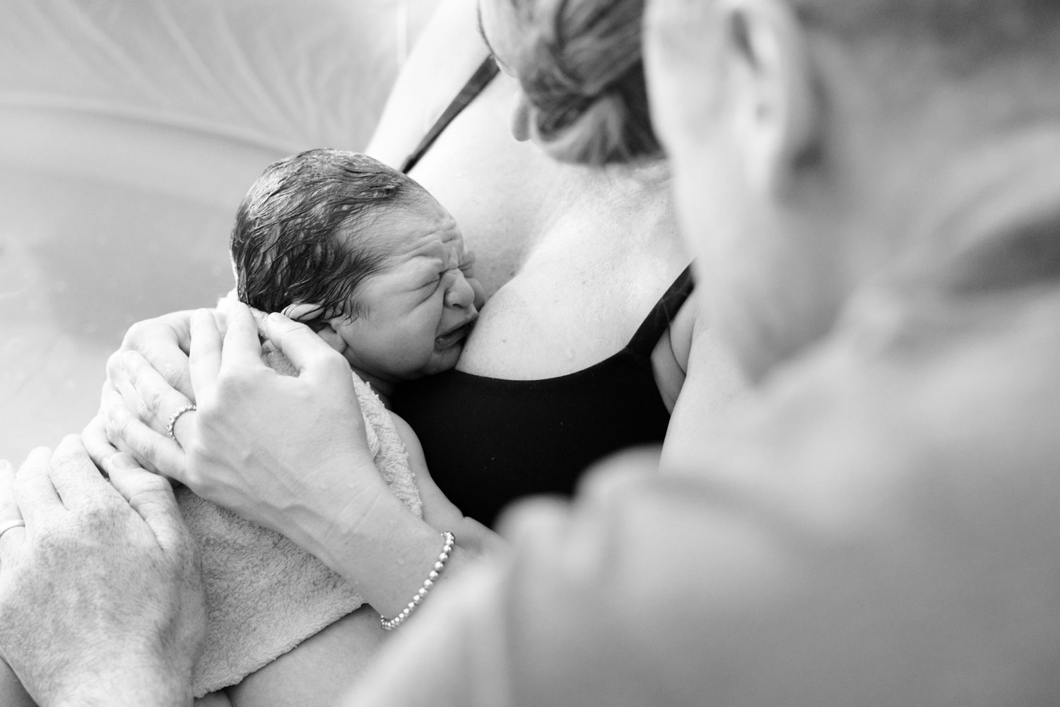 Tender moment as newborn baby rests against mother's chest wrapped in soft towel after birth.