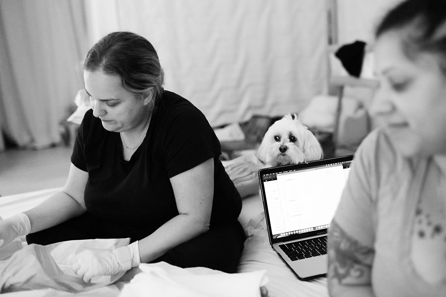 Black and white photo of two midwives working with a laptop and medical supplies during a home birth.