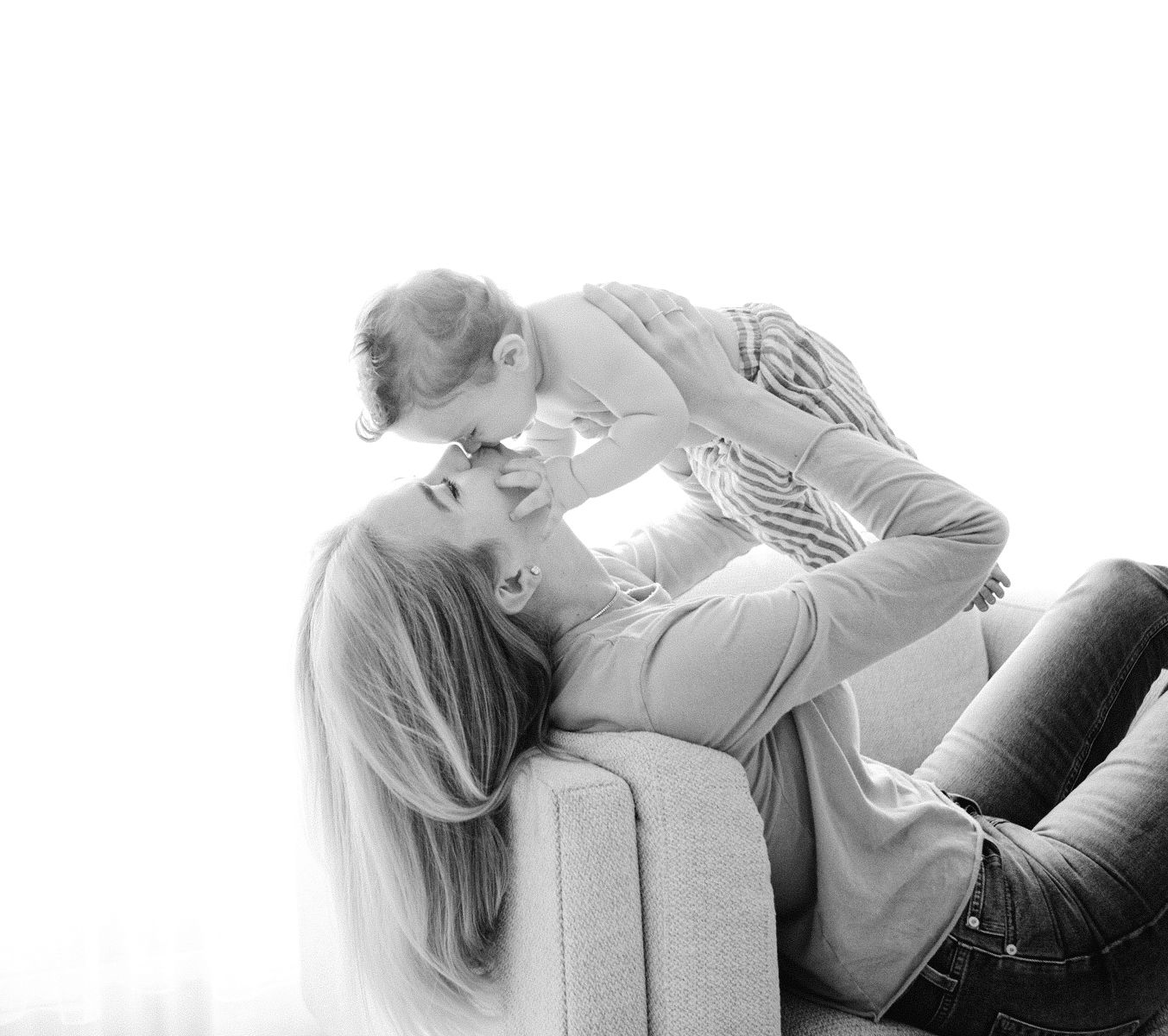 Black and white photo of a mother lying back lifting her baby in the air, sharing a tender moment.