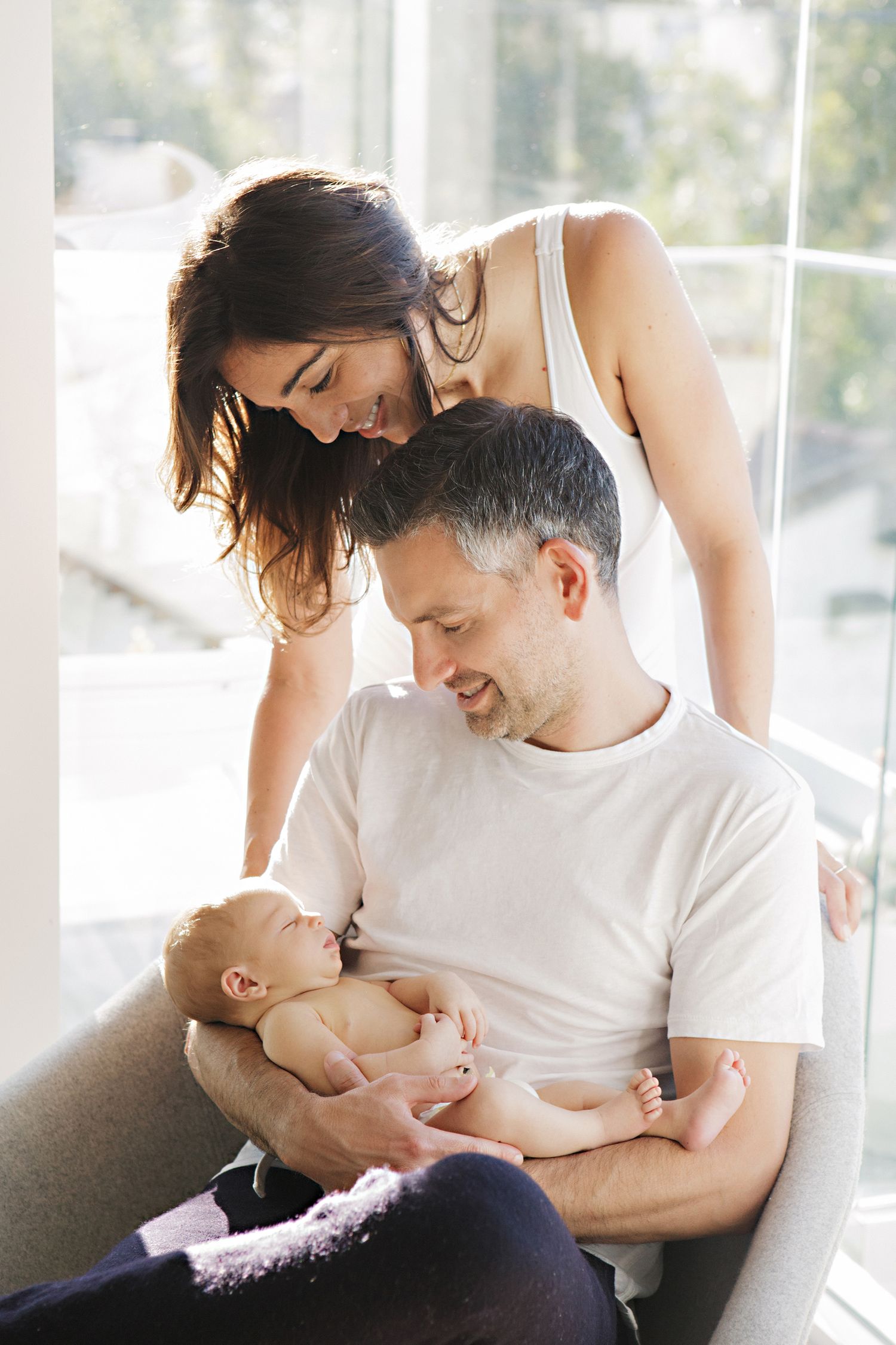 Happy parents smiling at their newborn baby, father holding infant while mother looks on lovingly indoors.