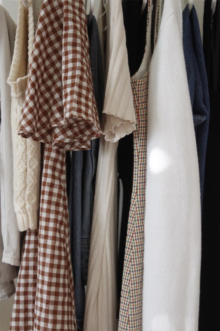 A clothing rack displaying neatly hung garments including brown gingham, cream knit, and navy pieces in a minimalist wardrobe.