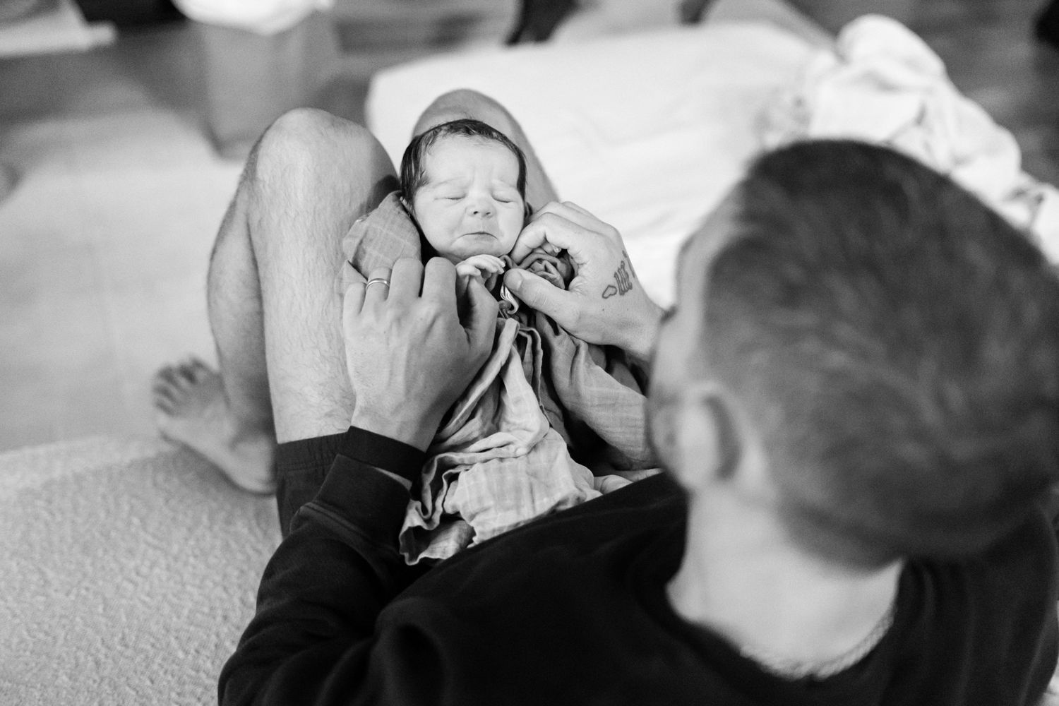Black and white photo of a father cradling his sleeping newborn baby on his lap.