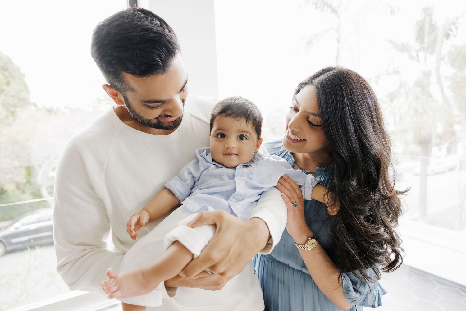 Happy young family with mother and father holding smiling baby in bright modern home setting.