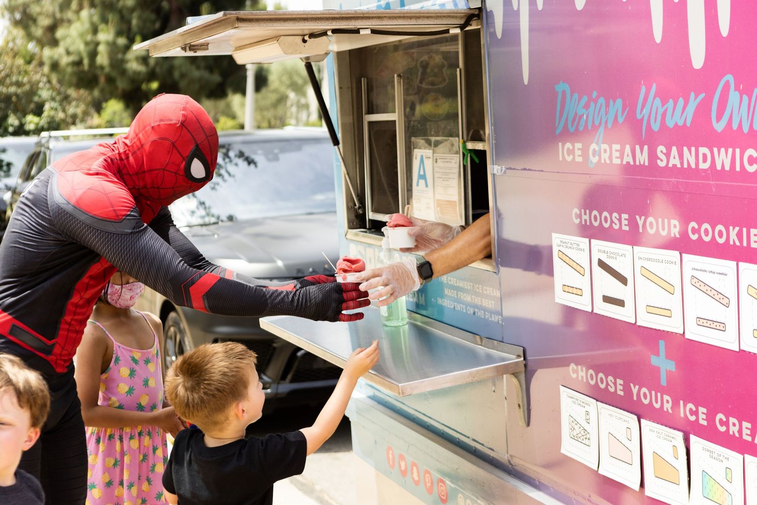 Person in Spider-Man costume handing ice cream to children at a custom ice cream sandwich food truck.
