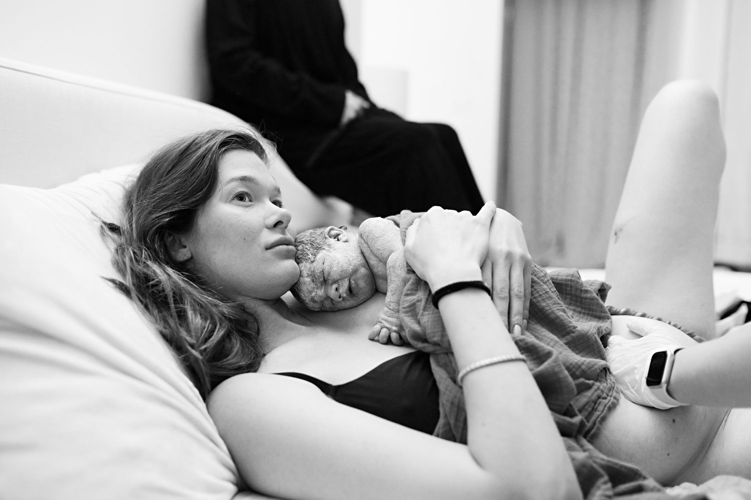 Black and white photo of a new mother lying in hospital bed, tenderly holding her newborn baby after childbirth.