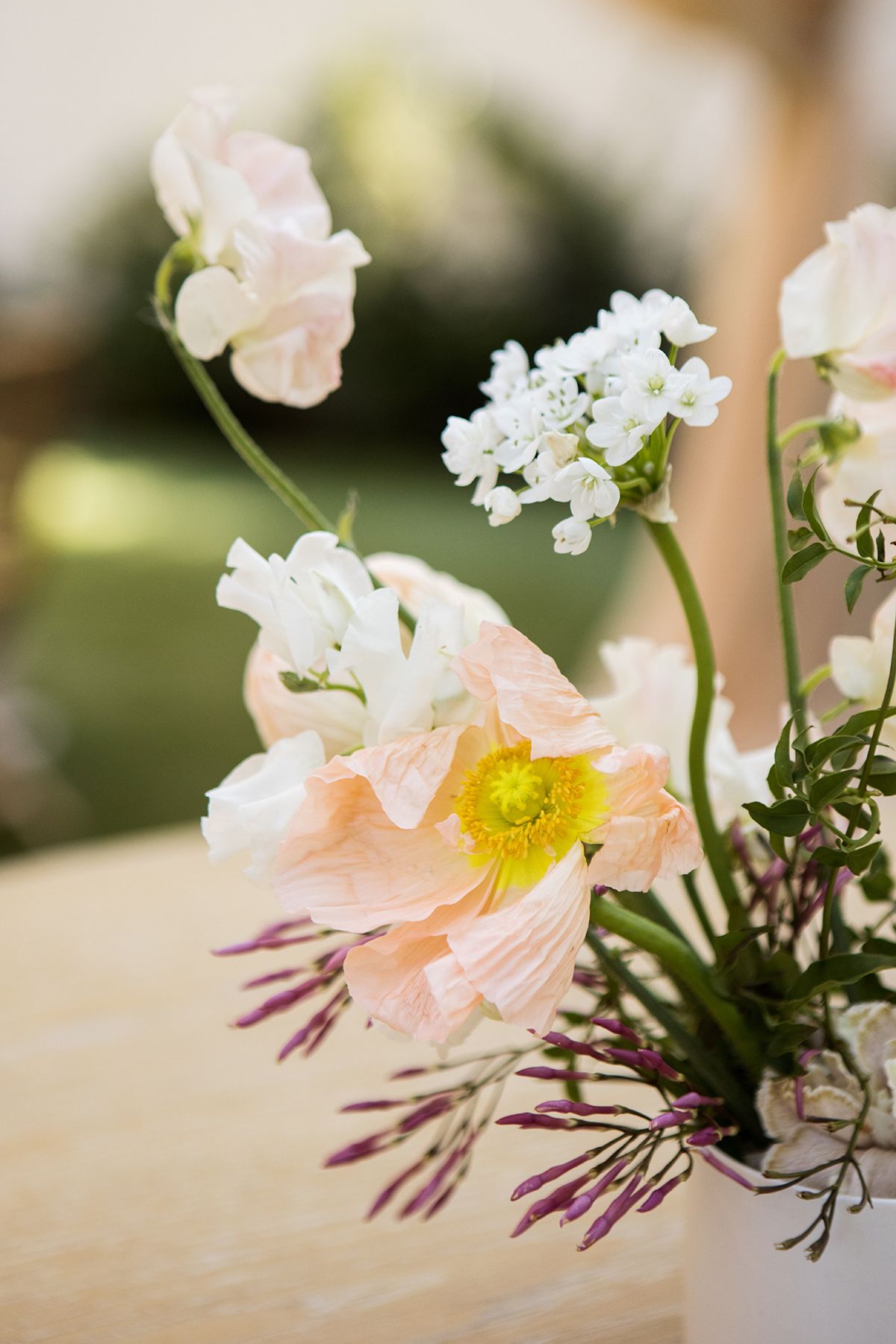 Close-up of soft peach poppy and white flowers in a bridal bouquet arrangement with green foliage outdoors.
