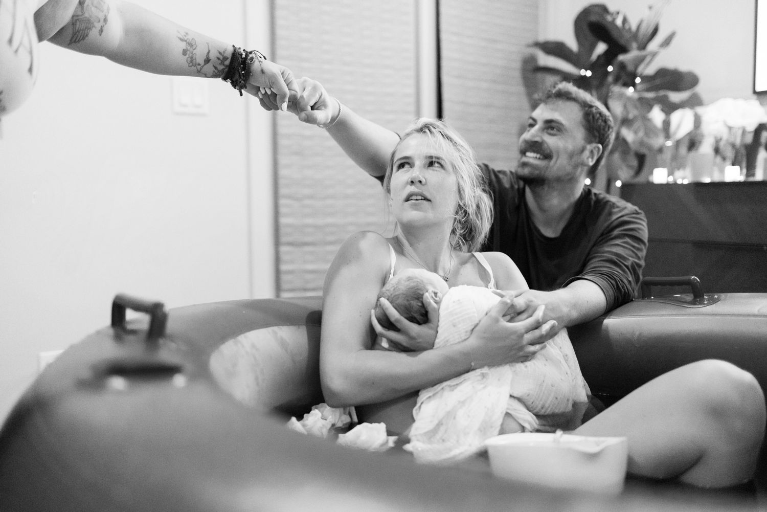 Black and white photo of new parents with newborn looking up joyfully at support team after water birth.