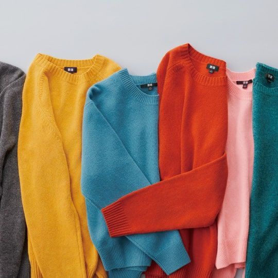 Colorful knit sweaters in gray, yellow, teal, orange, and pink arranged overlapping on a light background.