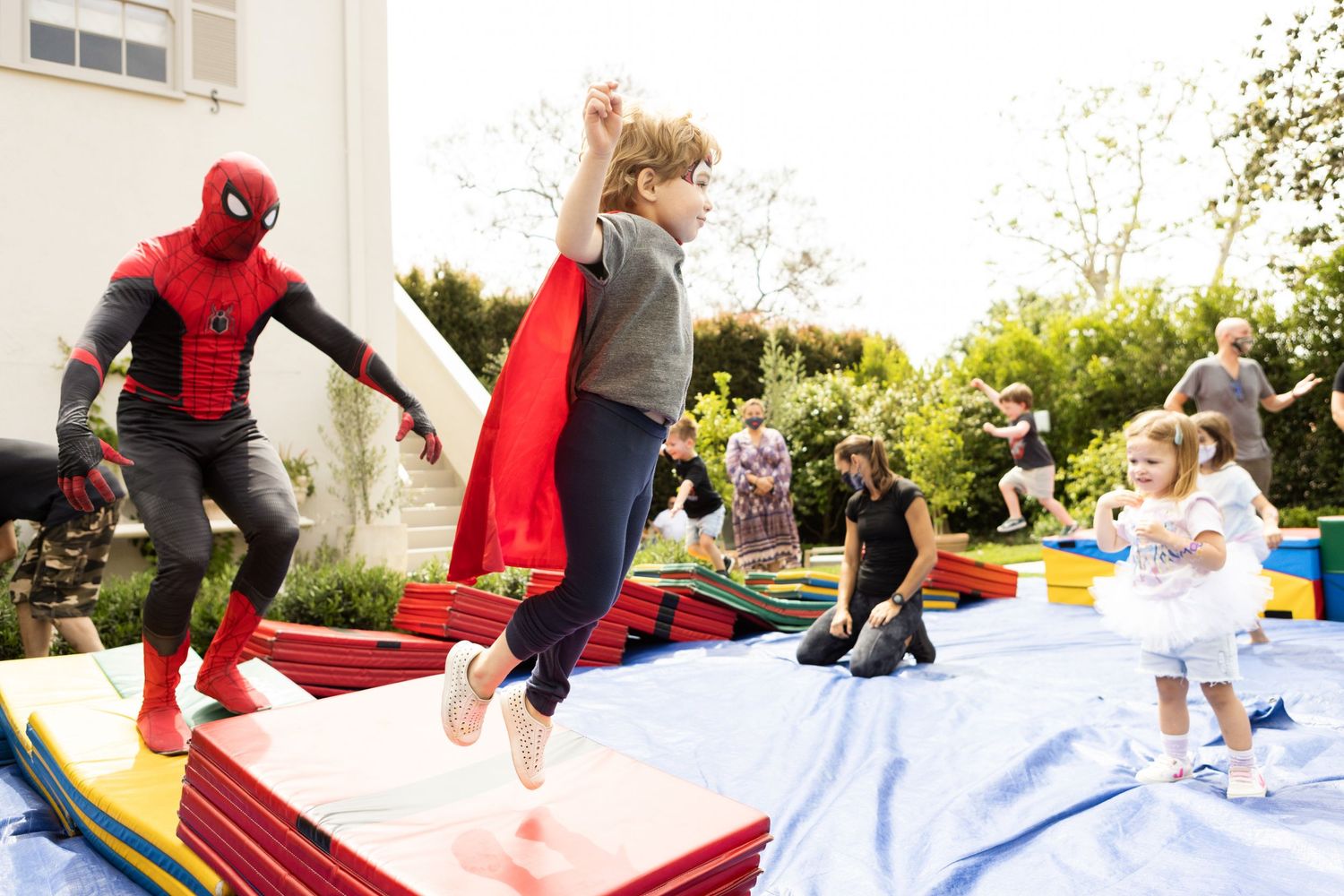 Children jumping on inflatable with Spider-Man costume character at a colorful outdoor birthday party.