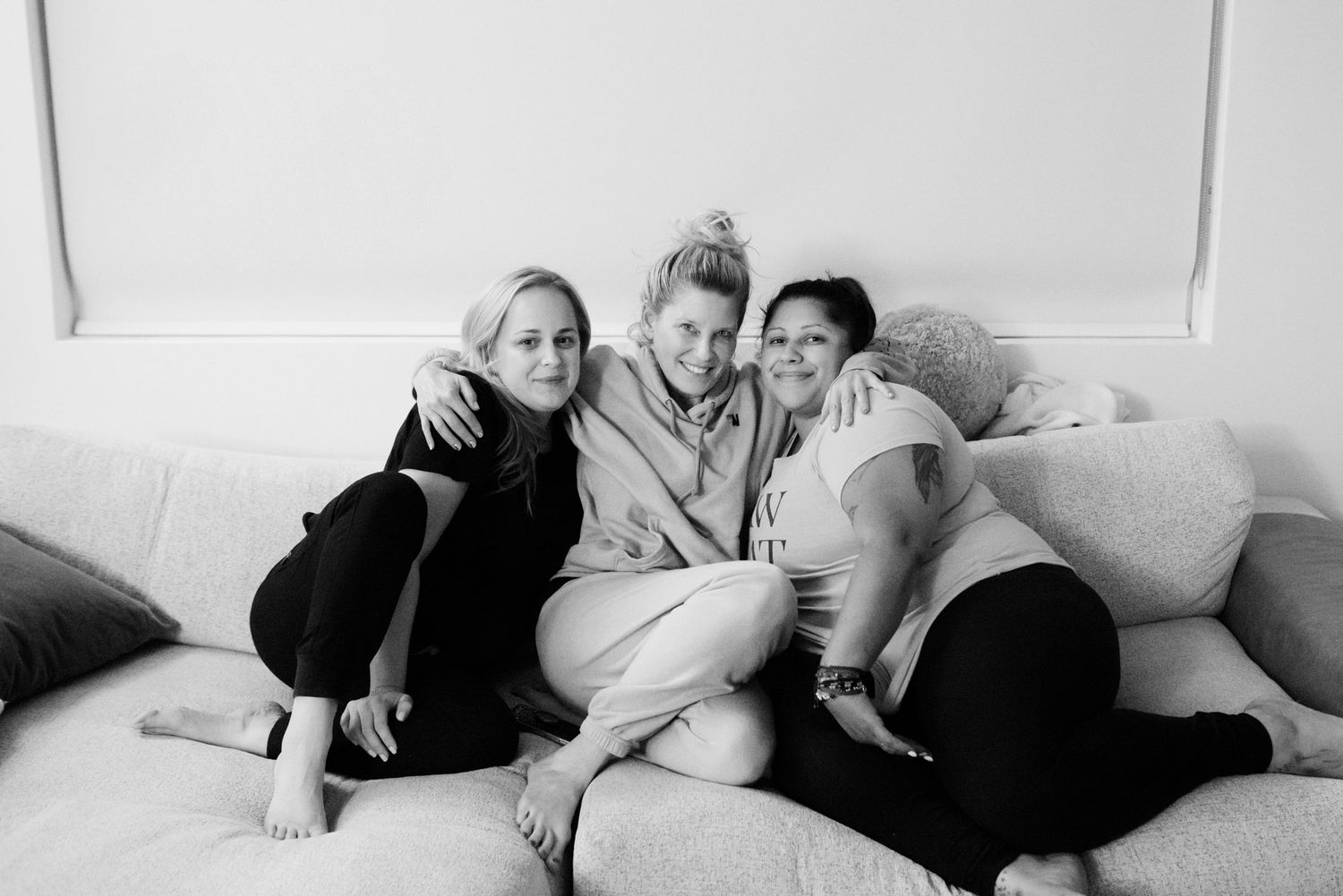 Black and white portrait of three smiling women sitting together on a couch after a home birth.